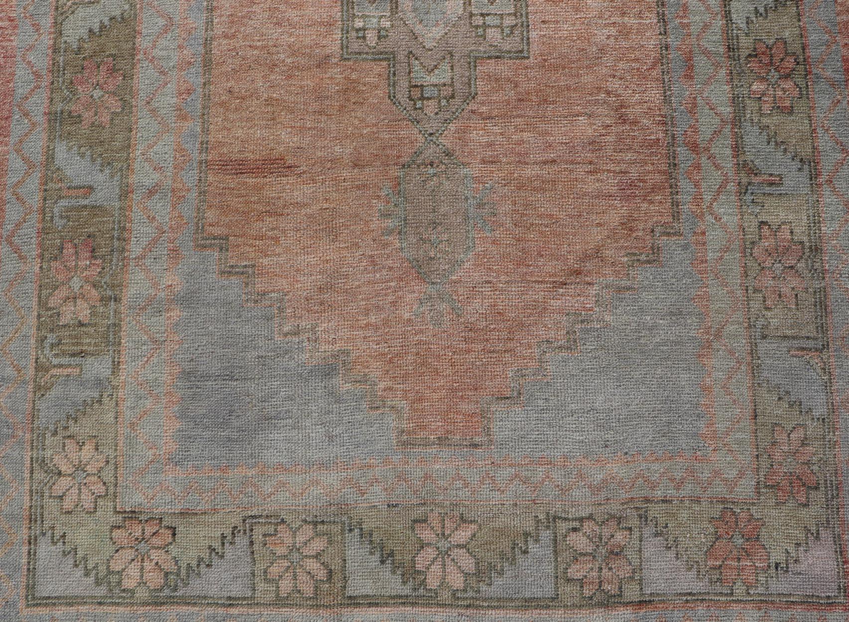 Measures: 4'7 x 11'2 

This vintage Turkish Oushak features large tribal medallions in light blue and tan. The medallions are decorated in tribal motifs and a peachy background. The border is a repeating tribal motifs and floral motifs with tan,