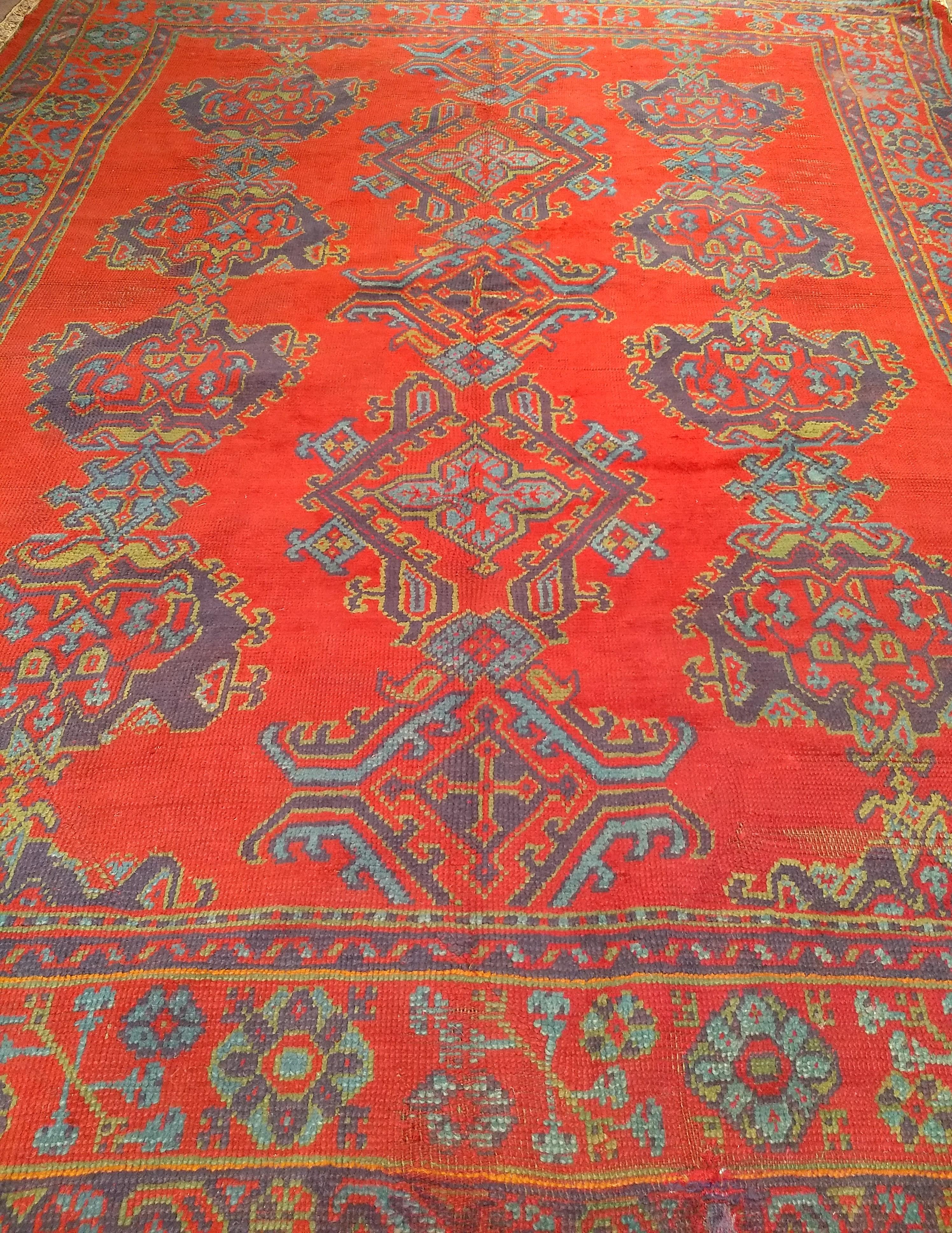 Début du 20e siècle, Oushak turc noué à la main  Tapis de taille ambiante avec un design all-over sur un beau et riche fond rouge. Il y a trois colonnes de grands motifs géométriques dans les couleurs bleu, vert, violet et jaune qui sont éparpillés