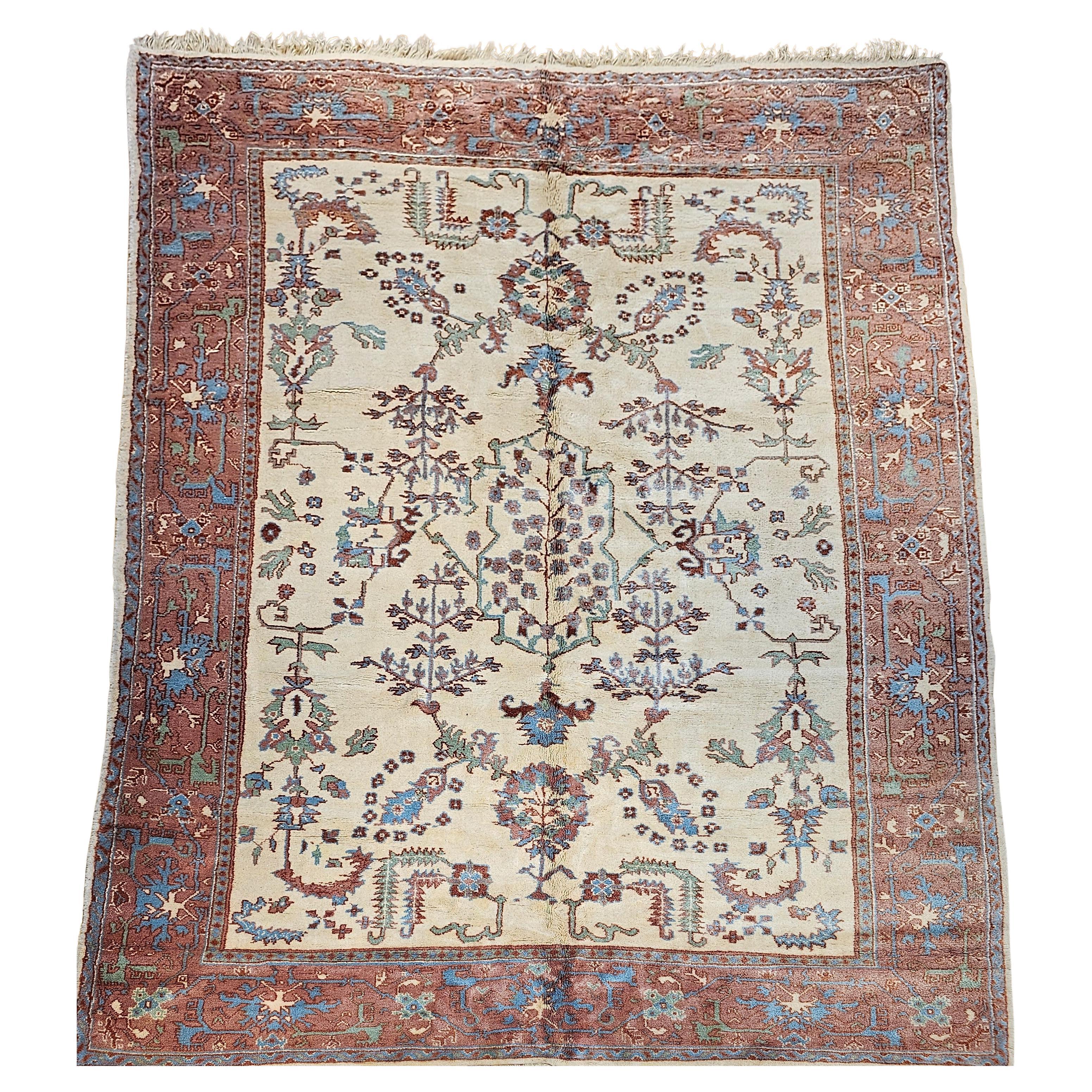 Beautiful vintage mid-1900s Turkish Oushak in an allover geometric design in an ivory color background with accent colors in torquoise blue, green and brown. Larger design forms of branches and leaves are scattered throughout the field and the