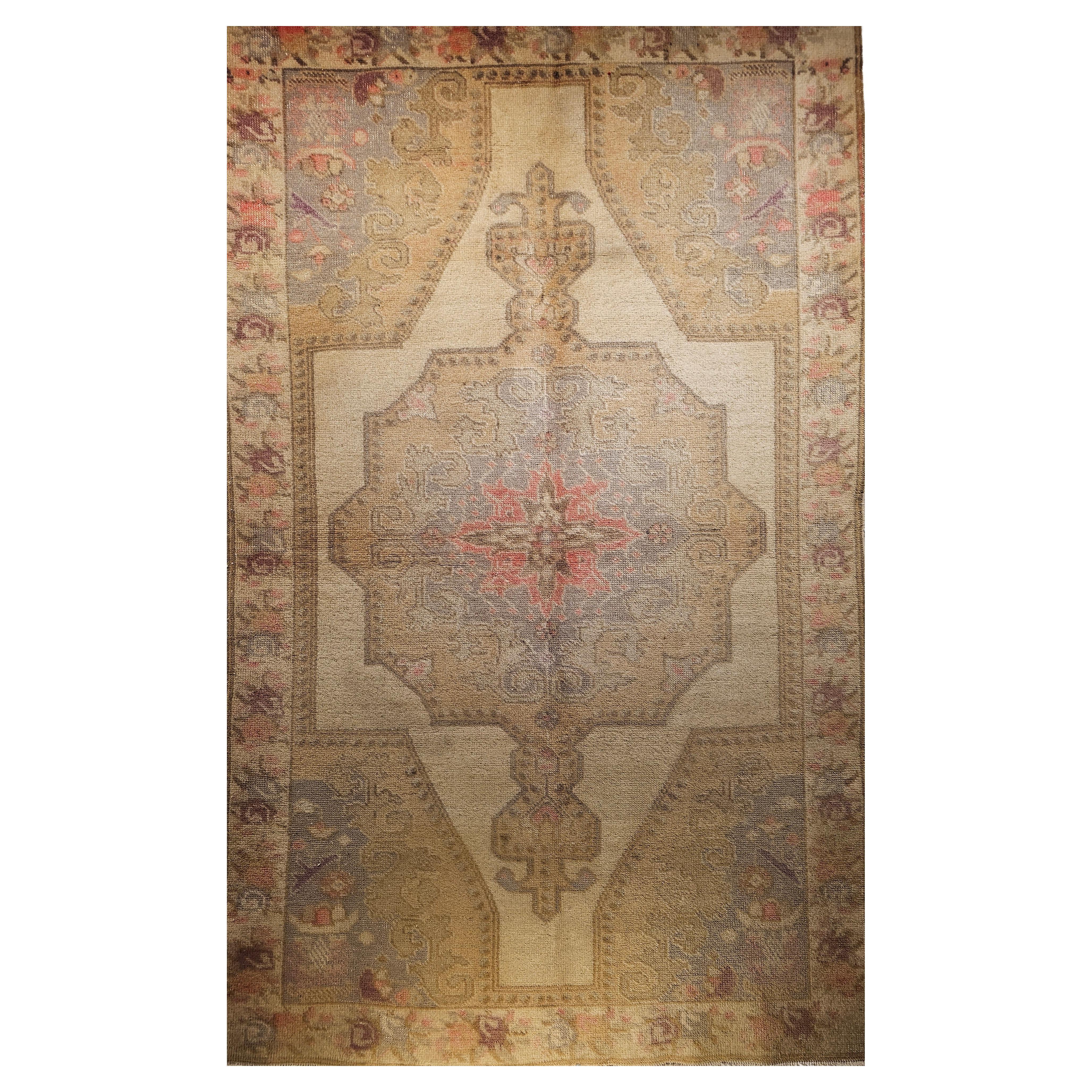  A vintage Turkish Oushak area rug with soft colors including pale yellow, pink, purple, and green from the early 1900s.  The rug has a beautiful open field design with an abrash pale yellow, purple, green and pink colors.  The corner spandrels are