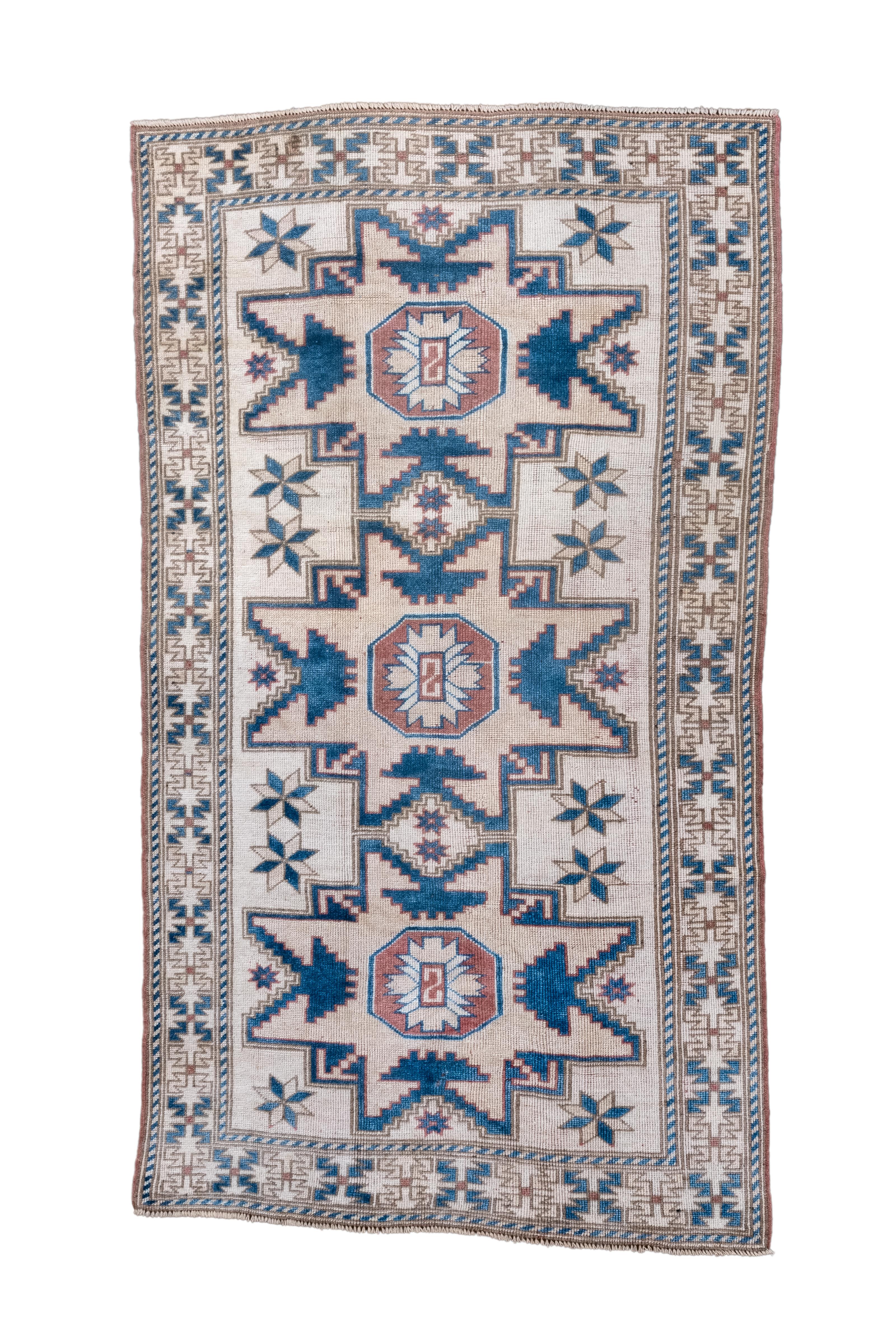 Sur un champ de sable clair, il y a trois grandes étoiles Lesghi bleu moyen et paille sable, toutes avec de petits octogones focaux rouille. Des étoiles apparaissent dans les réserves autour des grands motifs.  Bordure crème de modules de quatre S