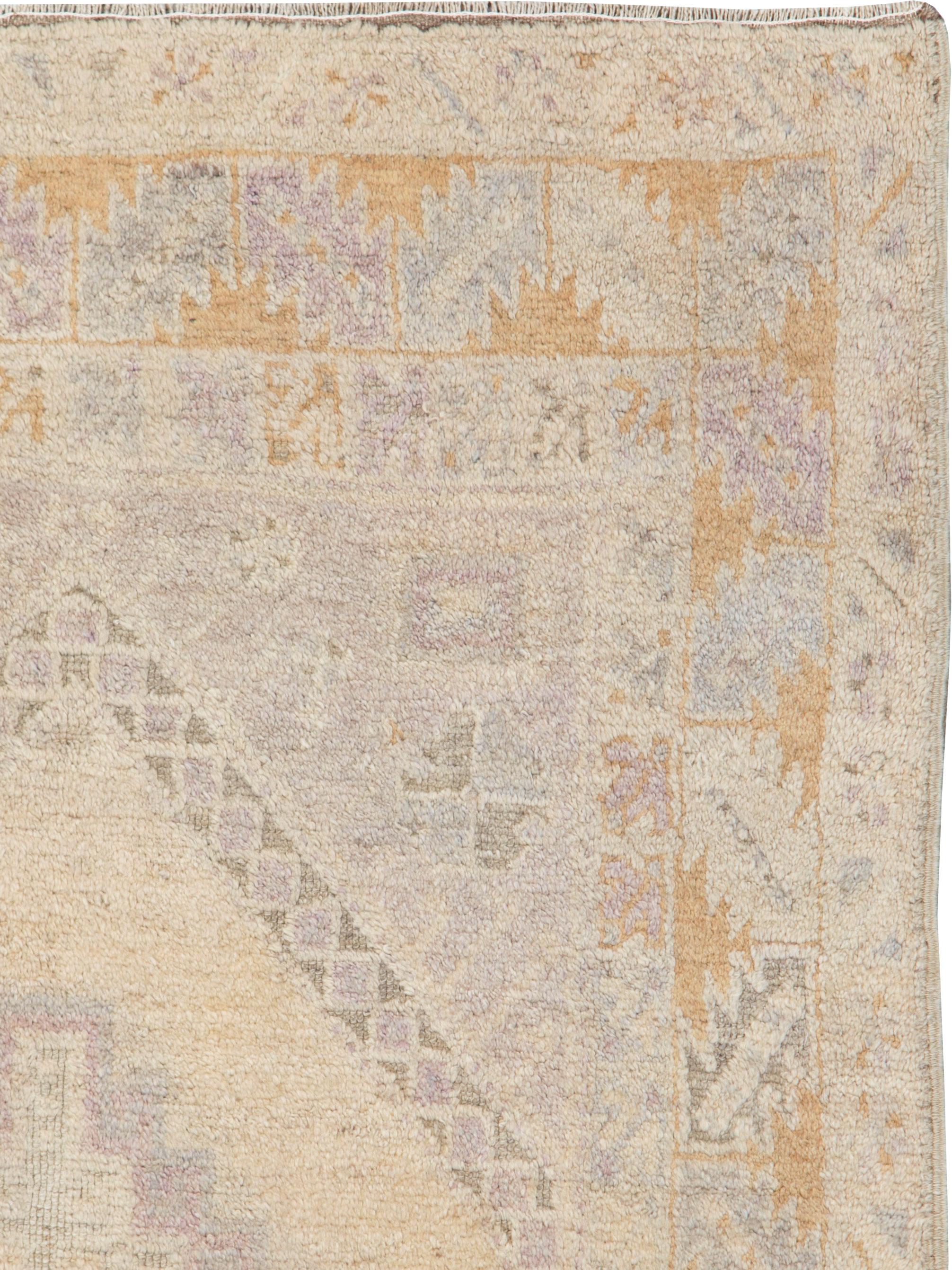 A vintage Turkish Anatolian rug. An overall soft palette dominates this rustic scatter with a soft beige hexagonal field centering a stepped beige and purple medallion. Rust-gold half ashiks decorate the main border of this subdued Anatolian