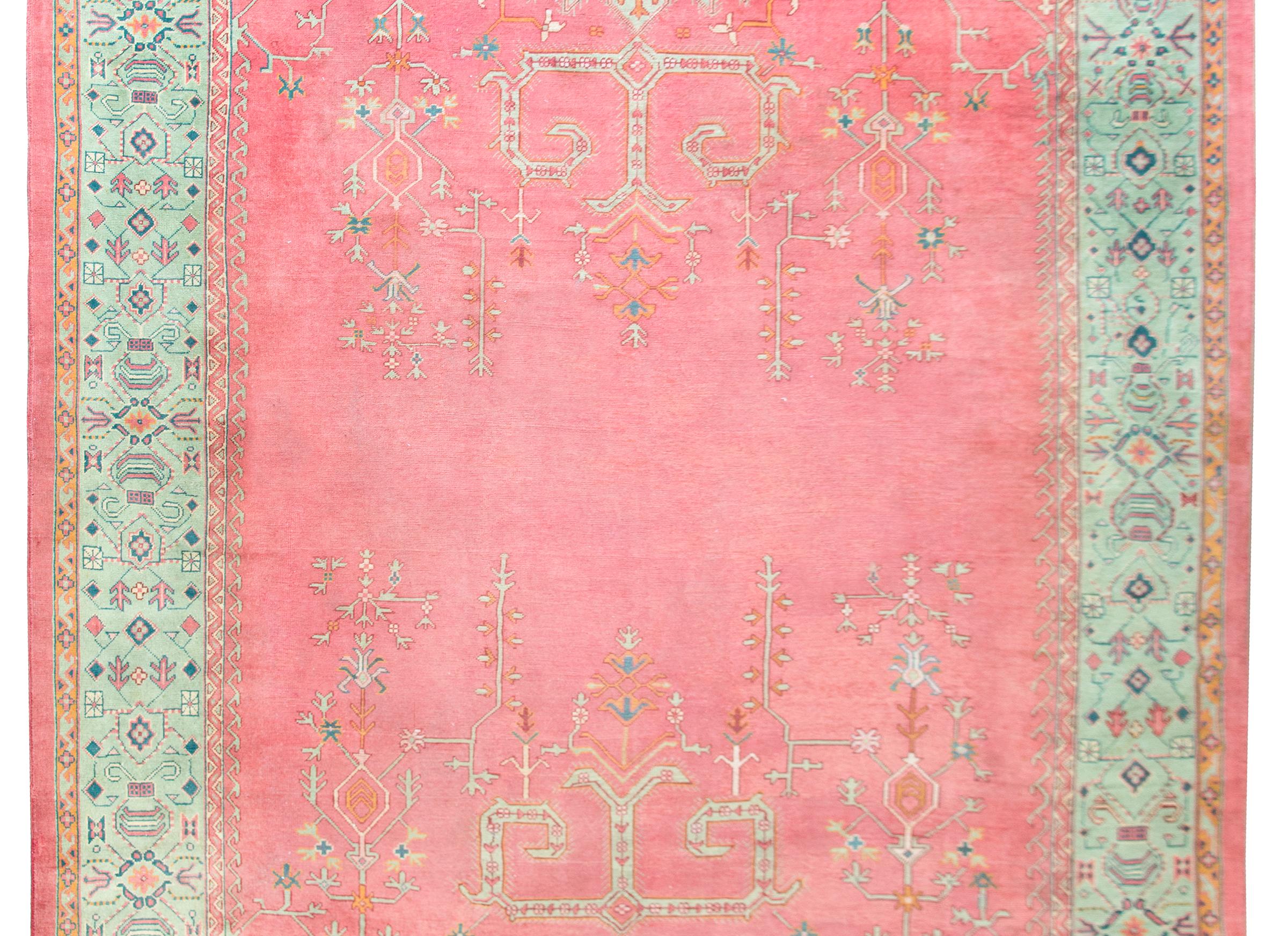 A brilliant early 20th century Turkish Oushak rug with a beautiful pink field overlaid with turquoise, orange, and indigo stylized scrolling vines and flowers, and surrounded by a wide border with more large-scale flowers and scrolling vines.