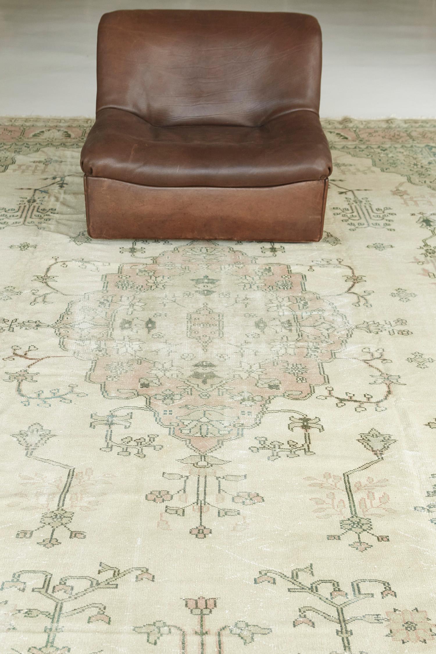 A stylish Vintage Oushak rug in the cool tones of ecru, rose, ocean green, stylized gracefully with majestic botanical details. Boasting its central medallion made of alluring blossoms and meandering vines, this beguiling rug from hand spun wool is