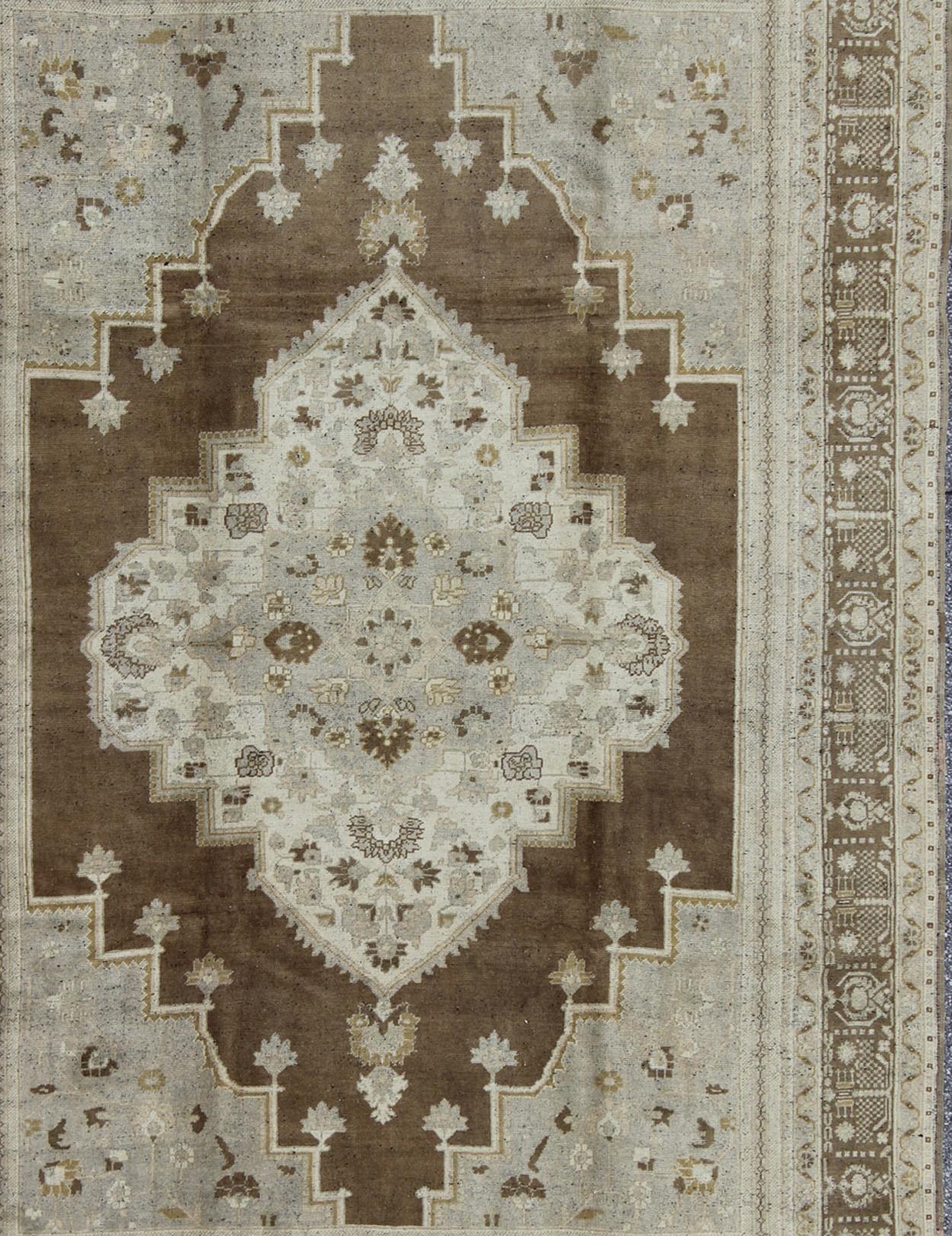 Measures: 7'4 x 11'4

This lovely Turkish Oushak from the 1940's features a central medallion, which rests on a dark brown background, is surrounded by a light brown border, and is characterized by a color palette of ivory with gray, brown and green