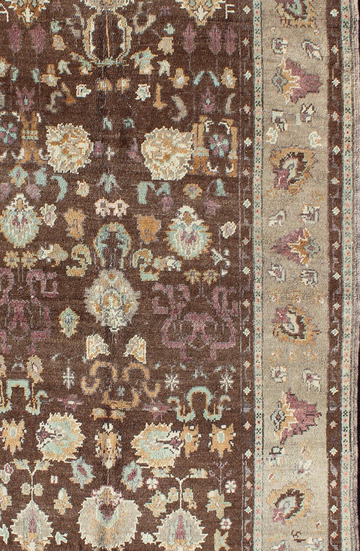 Measures: 4'5 x 8'3

This Turkish Oushak is set on a chocolate-brown background and features a light gray/taupe border. The overall palette remains cool, with accent colors of ice blue, shades of taupe-gray, creamy orange, burgundy and hints of