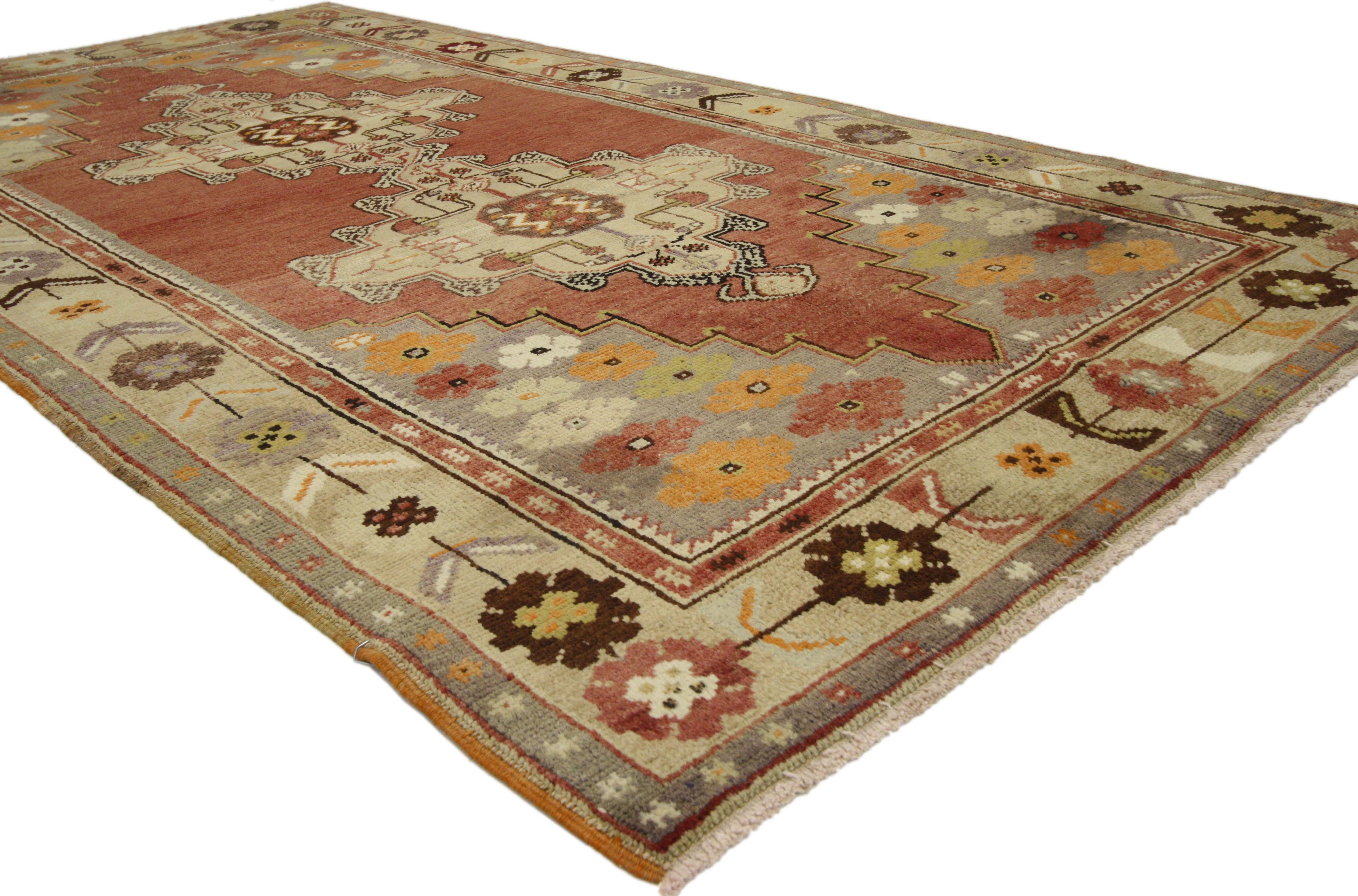 50122, vintage Turkish Oushak rug. This luxurious Oushak rug features two central medallions in geometric styles with plump fruits and delicate flowers topped with cruciform figures on a field of red. Slate spandrels sprout with delicate blooming