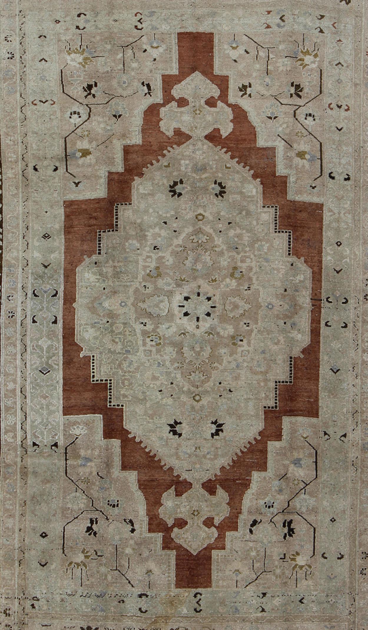Measures: 7' x 11'5

This beautiful vintage Turkish Oushak carpet features a sub-geometric design and a central medallion. The medallion features Sienna color which is surrounded by taupe, beige and very pale green tones, all surrounded by a