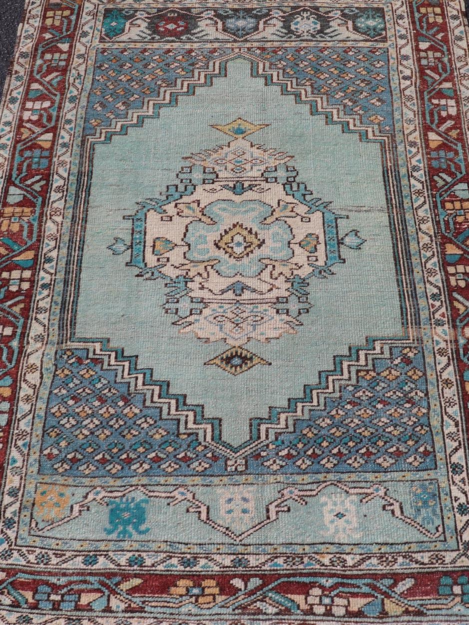 Medidas: 3'5 x 5'1 Esta impresionante alfombra turca Oushak Vintage presenta una vibrante paleta de verde azulado y granate intenso, bellamente combinada con intrincados motivos geométricos y florales. El campo central de la alfombra está dominado