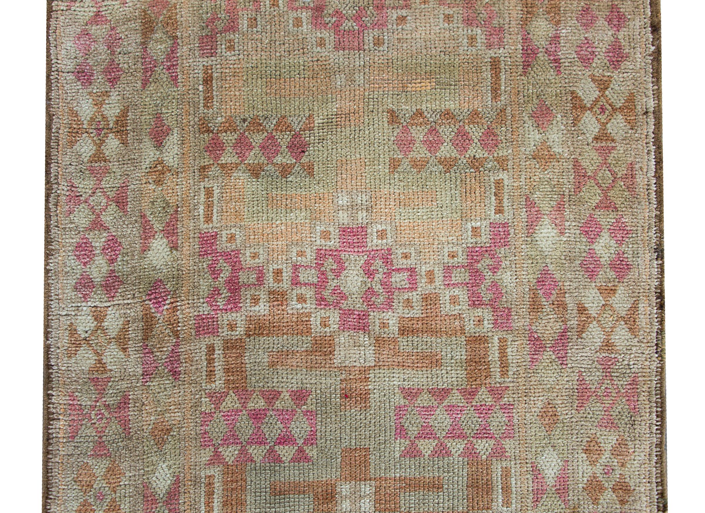 A simple yet chic Mid-20th Century Turkish Oushak rug with an all-over geometric pattern woven in muted pinks, golds, oranges, and natural colored wools, and all surrounded by a border of even more geometric patterns woven in similar colors and the