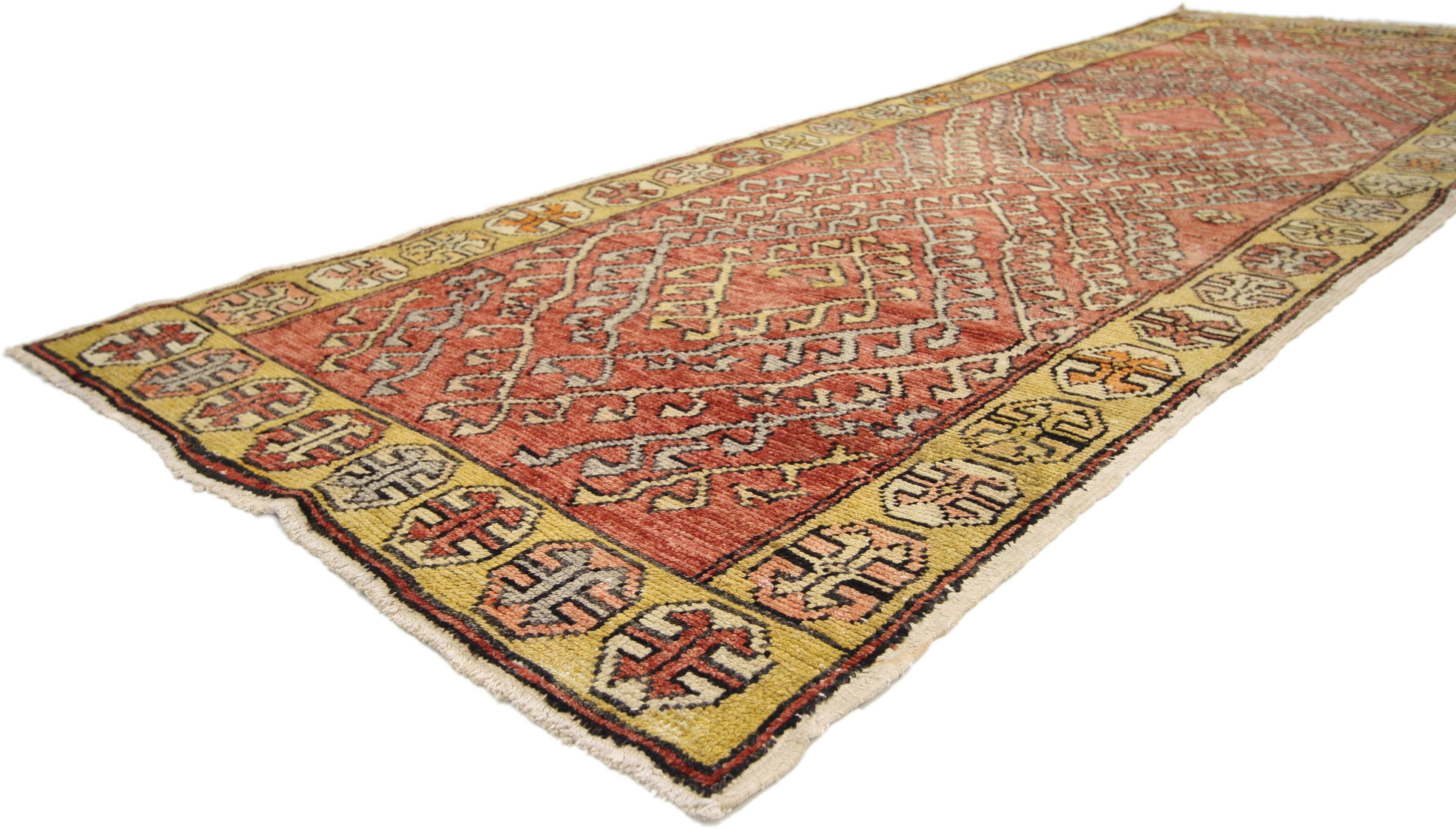 This hand-knotted wool vintage Turkish Oushak runner features a modern tribal style. The rich waves of abrash and eccentric design of this Oushak carpet runner showcase a highly decorative composition with time-softened colors. Rendered in