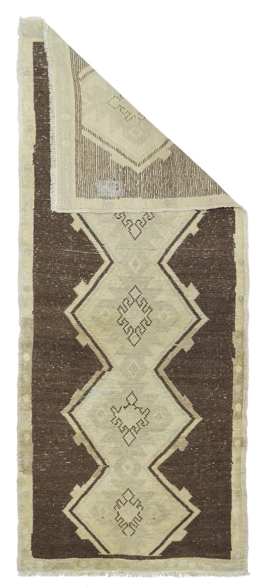Vintage Turkish Rug 2'7'' x 6'6''. Das leicht abgenutzte, umberbraune, offene Feld zeigt breite, quadratische Zickzacklinien, die eine zentrale, beigefarbene Reserve definieren, die fünf leicht hakenförmige Rauten einschließt. Einfarbig stroh-beiger