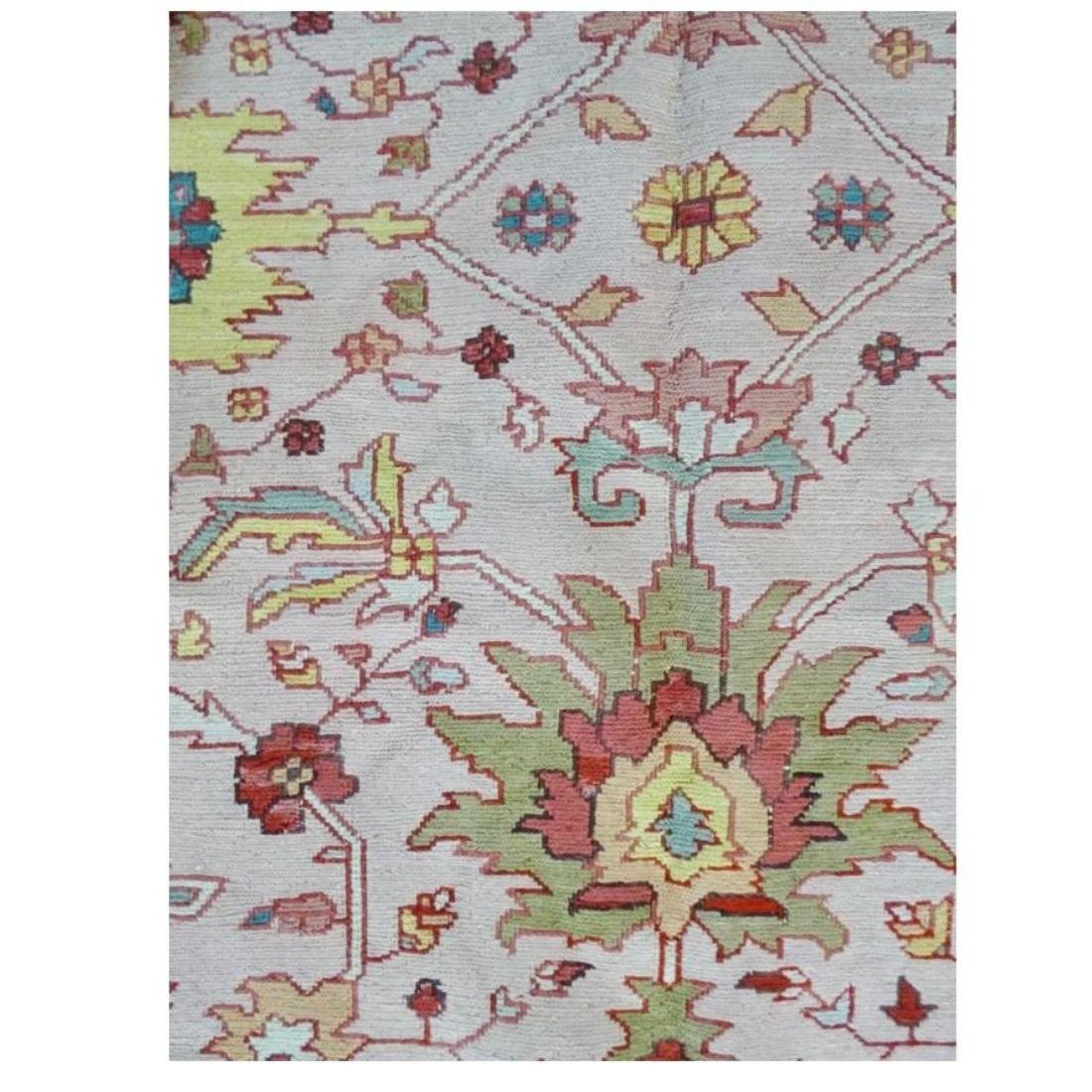 A vintage Turkish rug with pinks, yellow and cream the dominant colors and greens and blue highlights.  An all over floral and geometric design with a blue border and geometric florals repeated on a smaller scale.