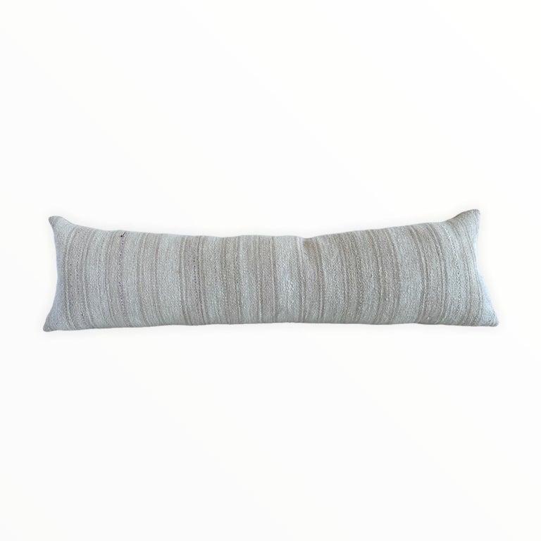 Vintage Turkish rug long lumbar pillow.
Size: 14” x 47”
Brass zipper closure, solid Belgian linen backing and down feather insert.
The face is a soft heavy woven rug in a light oatmeal color and pale faded blush, and taupe stripe.
 