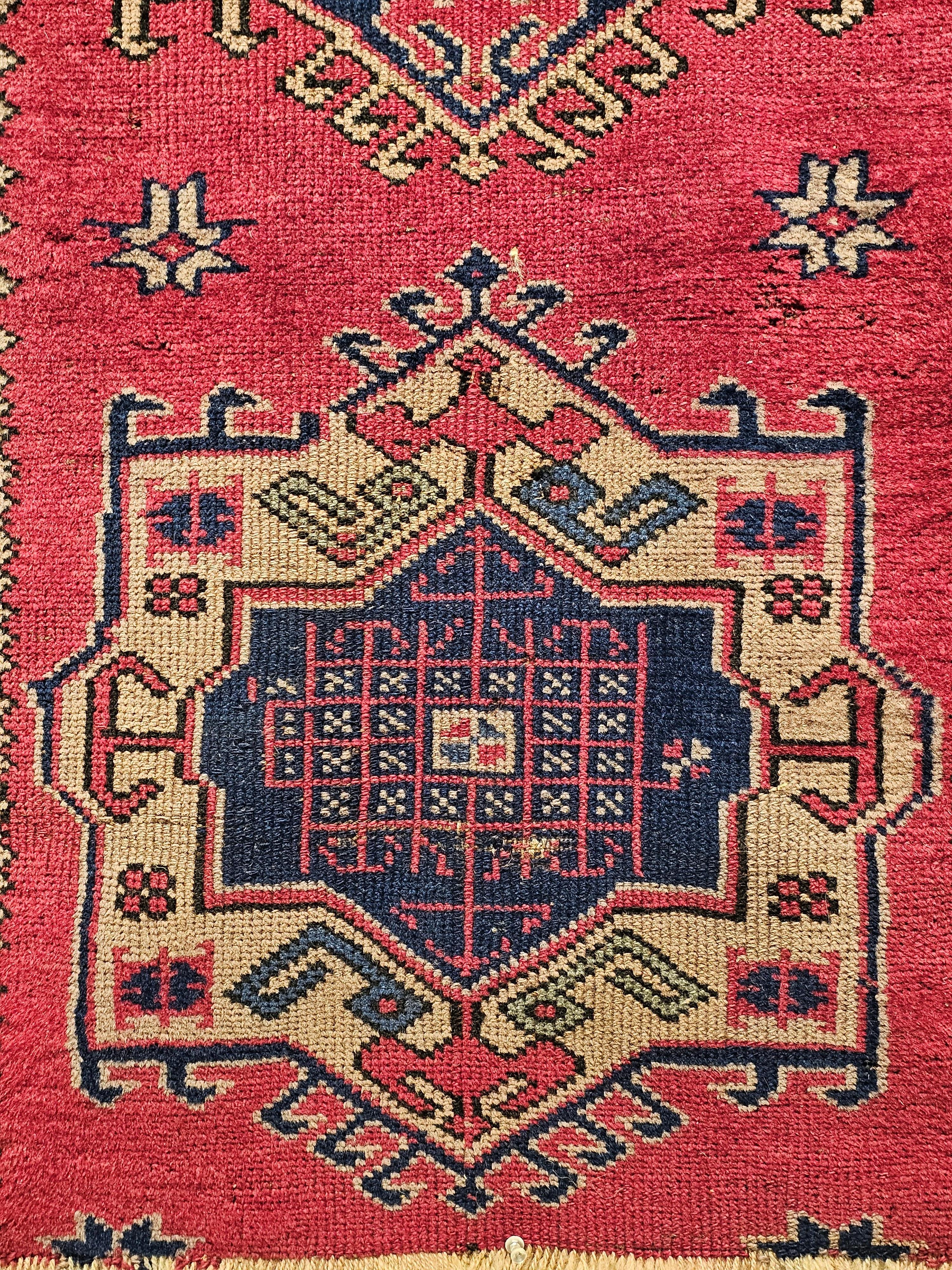 A Turkish village runner in a geometric medallion design similar to the Persian Heriz Karajeh runners.  The runner has a red background with four medallions in alternating colors of  ivory and navy background and designs in green, blue, pink and