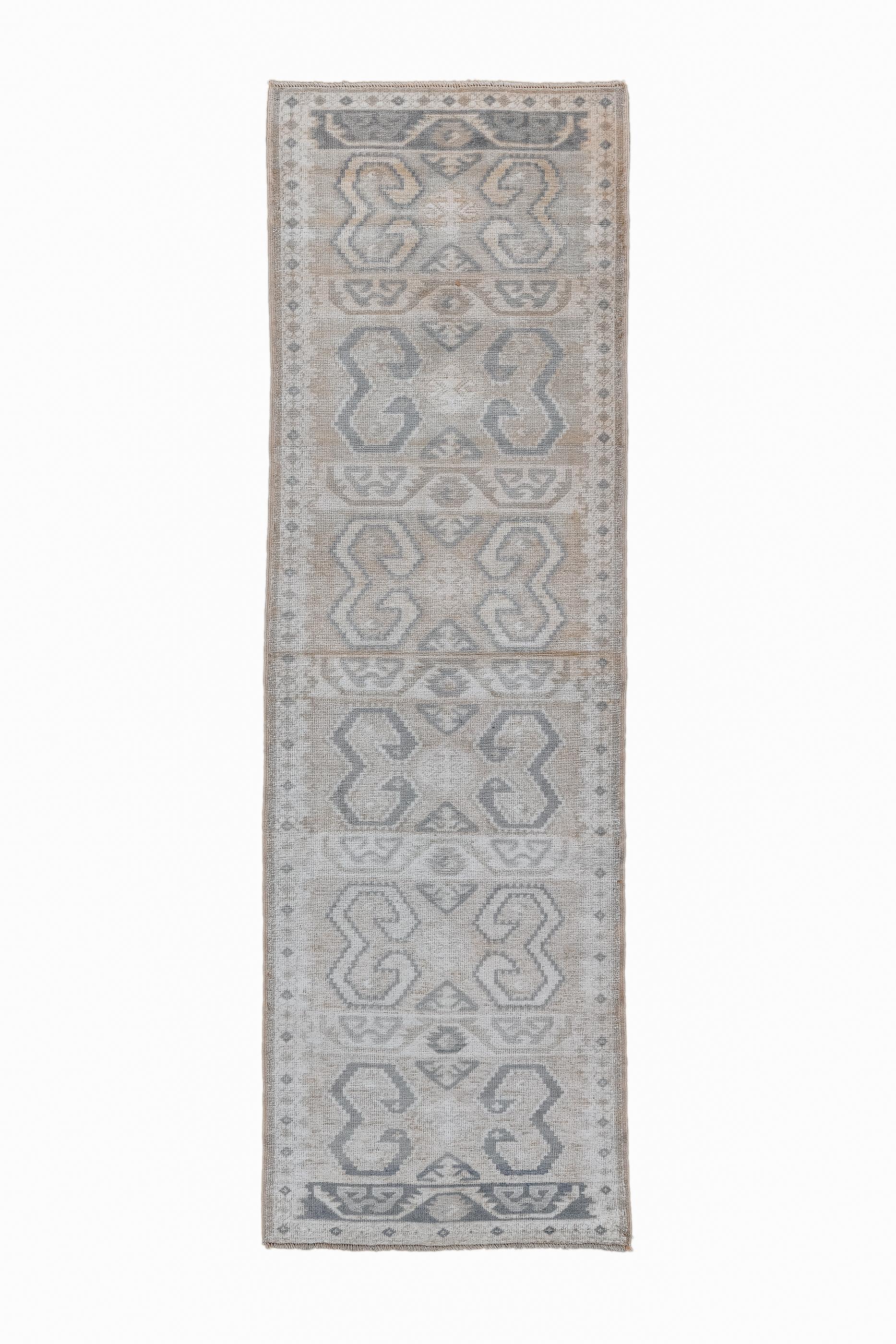 This softly toned little runner shows an eight panel design derived from kilims of bold pairs of rams’ horns. The tips of the volutes have “eyes” suggesting birds. Stepped outlines also refer to kilim sources. Small separator strips with trapezoidal