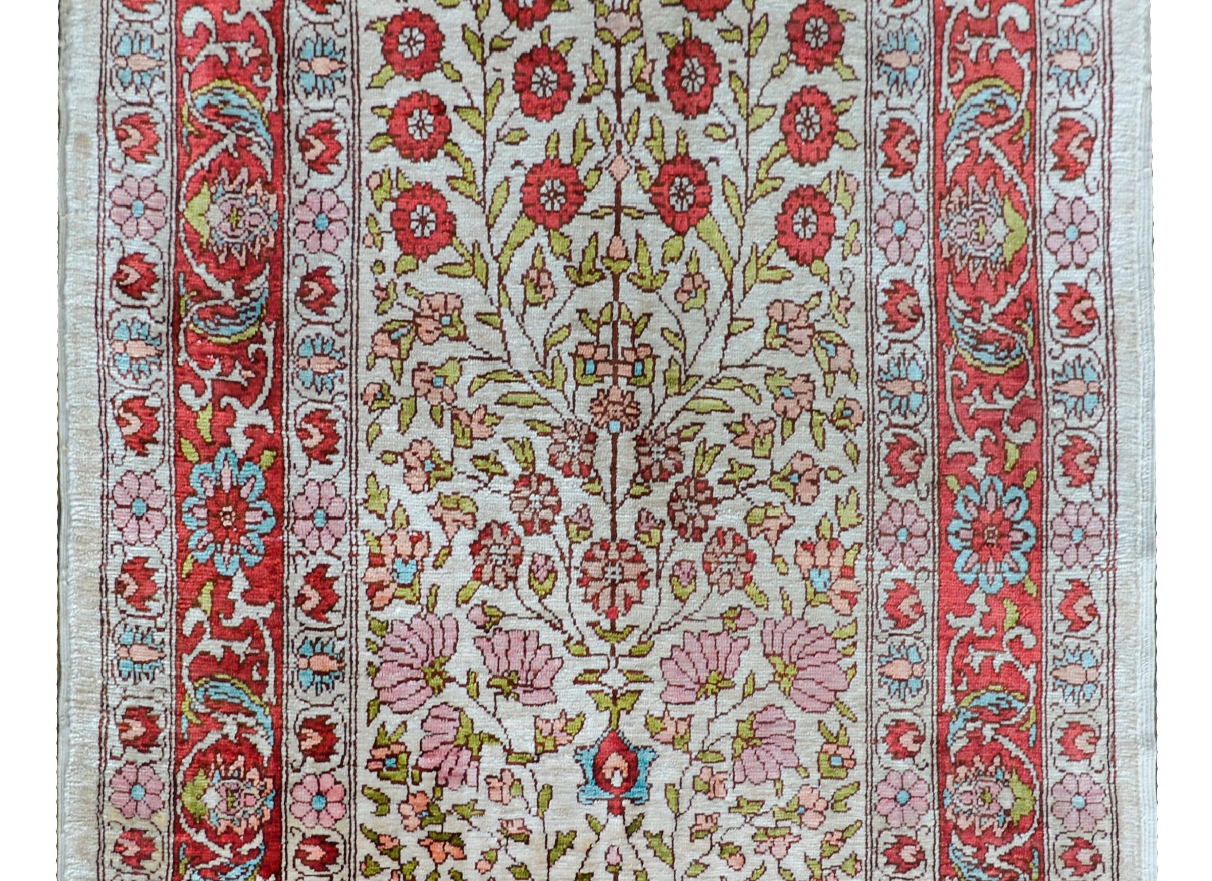 A wonderful vintage Turkish Hereke rug made from 100% silk, and woven with a beautiful multi-colored tree-of-life pattern in the center surrounded by a wide borer containing multiple petite floral colored stripes.
