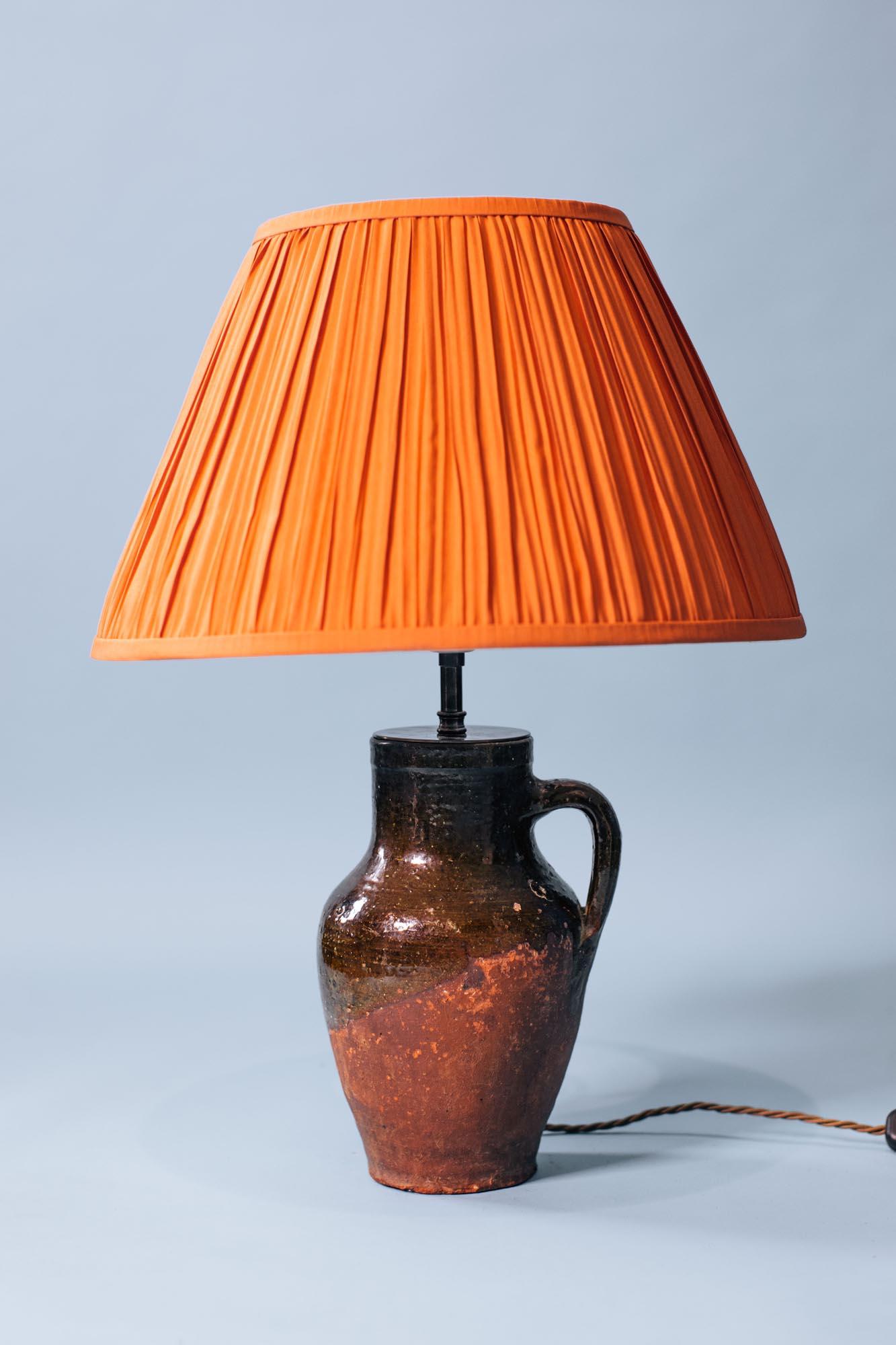 Lámpara de mesa vintage turca de jarra de terracota, fabricada a mano en el siglo XX con técnicas tradicionales de la alfarería de Anatolia. La lámpara tiene forma de jarra redondeada con una sola asa y una característica superficie esmaltada en