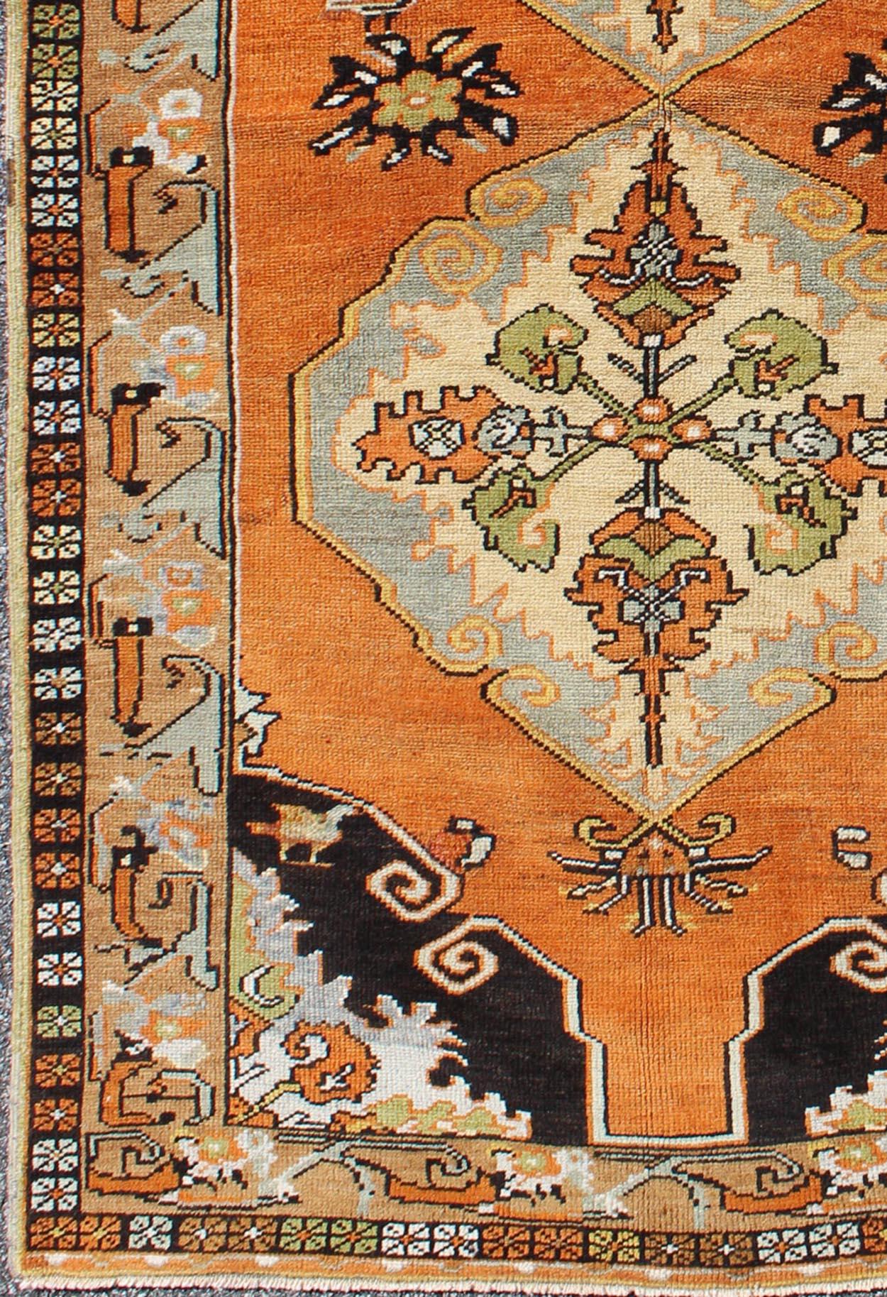 Measures: 3'9 x 6'5

This vibrantly colored Turkish Oushak features two medallions and a highly detailed design set on an orange background with dark brown and light taupe colors and stunning blue corner borders. The bold and geometric design is