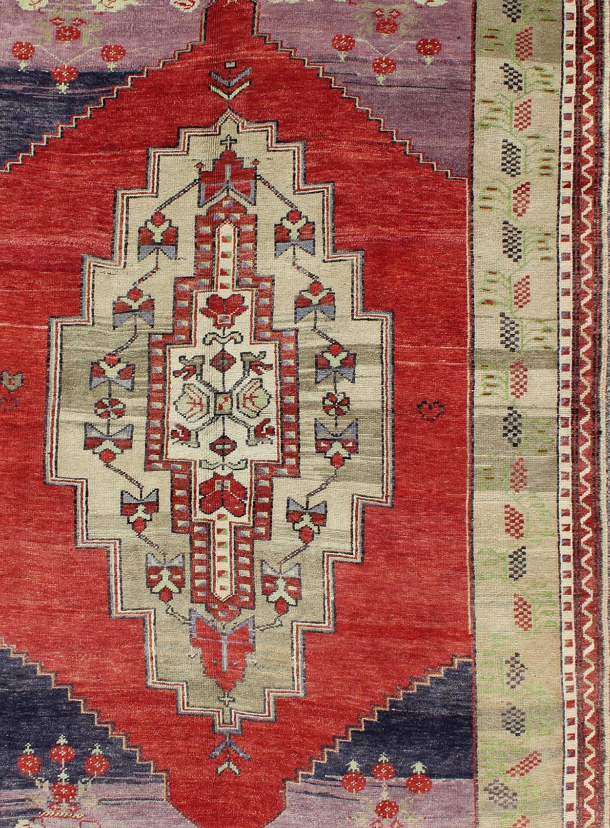This beautiful rug from mid-20th century Turkey features a classic Oushak design, large scale medallion in the field, rendered in red, champagne, and taupe. Each corner of the field is corniced with floral motifs atop lilac and dark blue. The