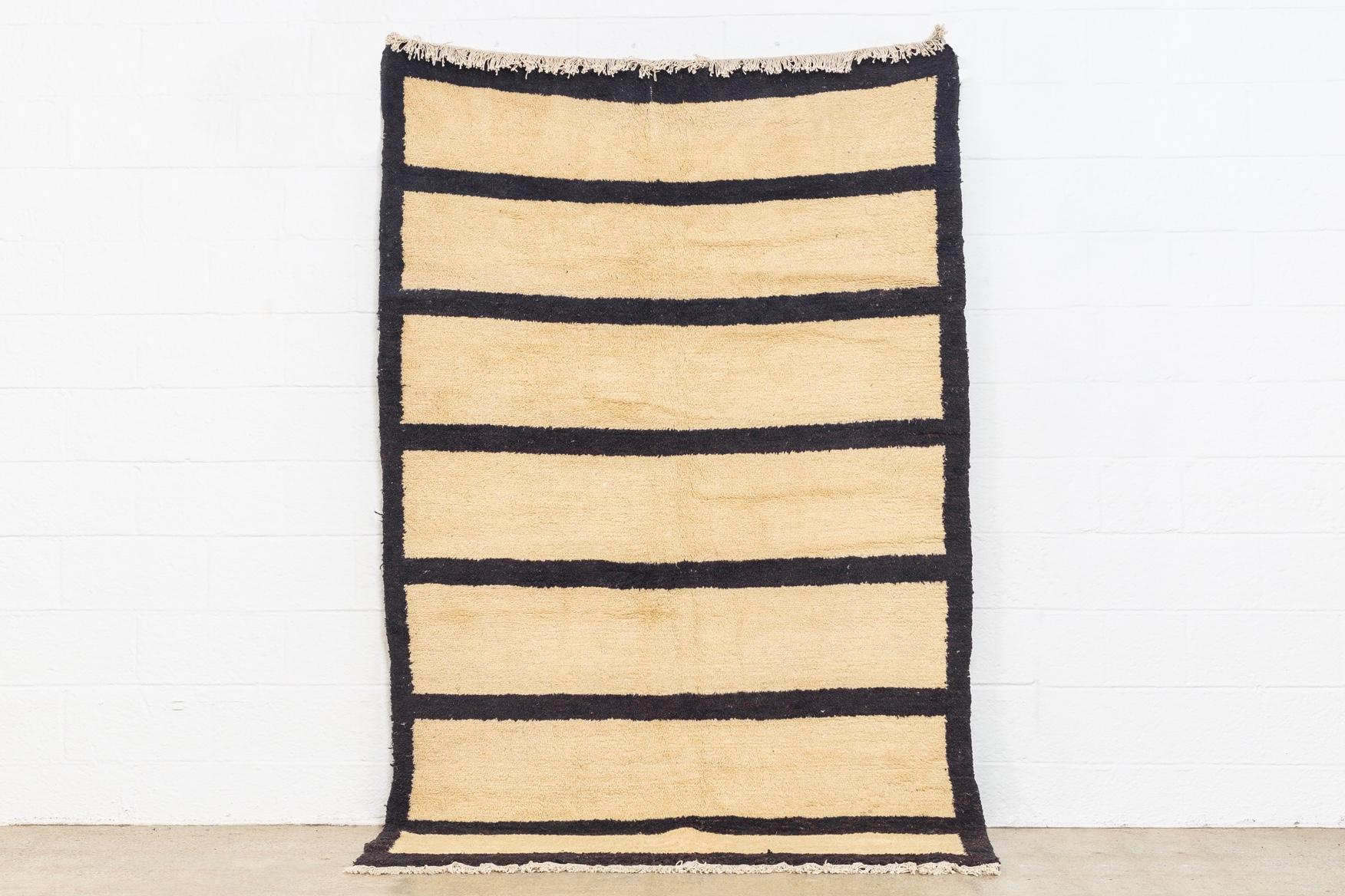 This vintage handwoven Anatolian Tulu wool floor rug features an abstract, Minimalist design with an open oatmeal tan field and dark brown stripes and border edge. The medium wool pile is finished with a natural cotton warp fringe to both ends. This
