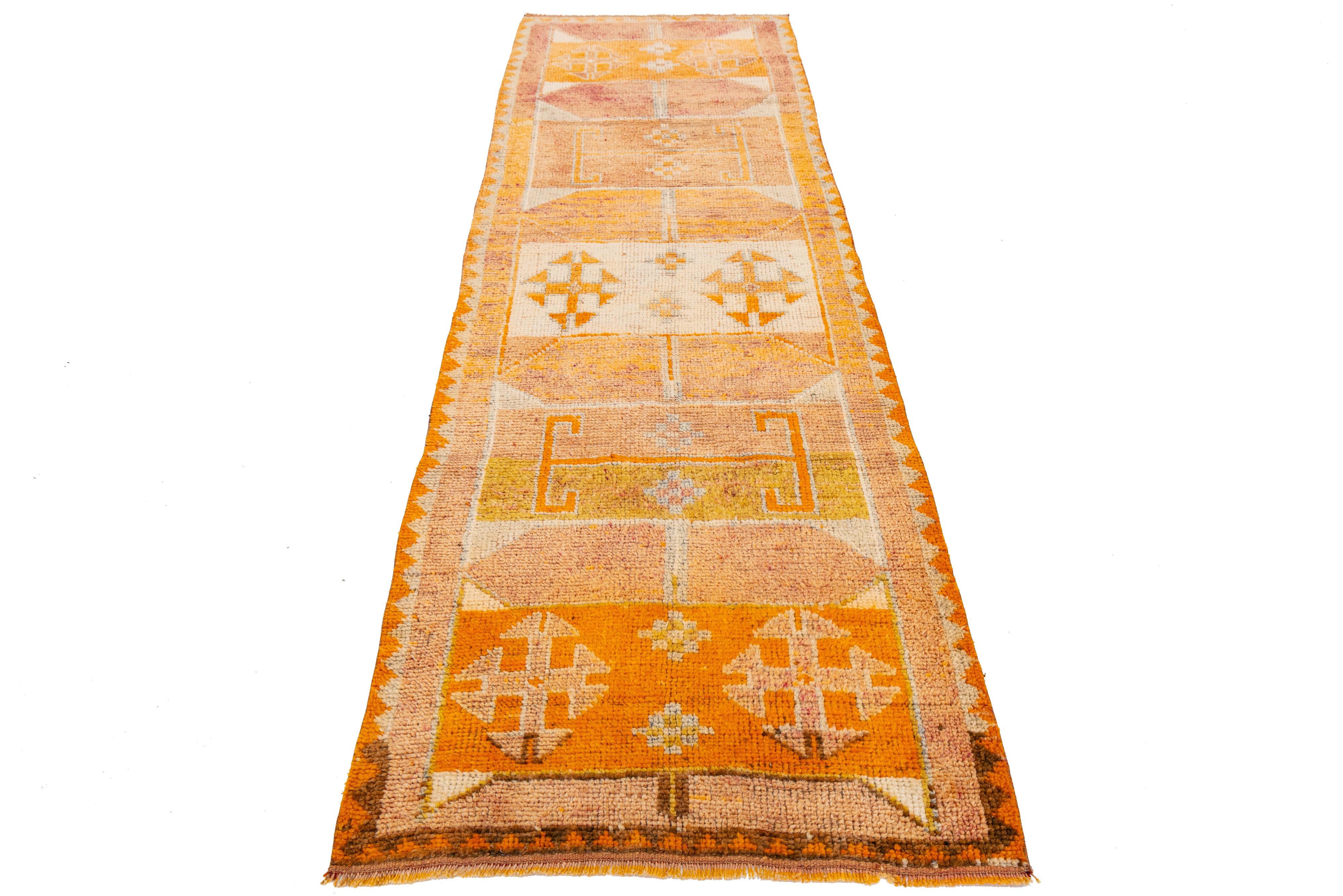 Handwoven in Turkey, this vibrant runner features three bold diamond medallions framed by stepped geometric patterns in warm tones of orange, ivory, and lavender. Inspired by traditional kilim designs, its symmetrical layout and natural wool texture