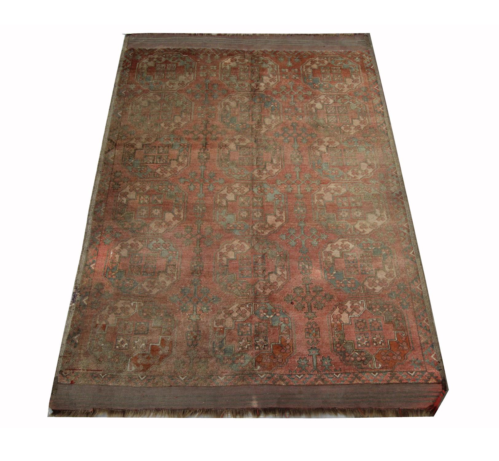 This vintage piece is a Turkmen Ersari rug in the 1940s. The central design features a rust background with a repeating traditional Turkmen medallion pattern that has been woven in accents of green and cream. The intricate designs and patterns woven