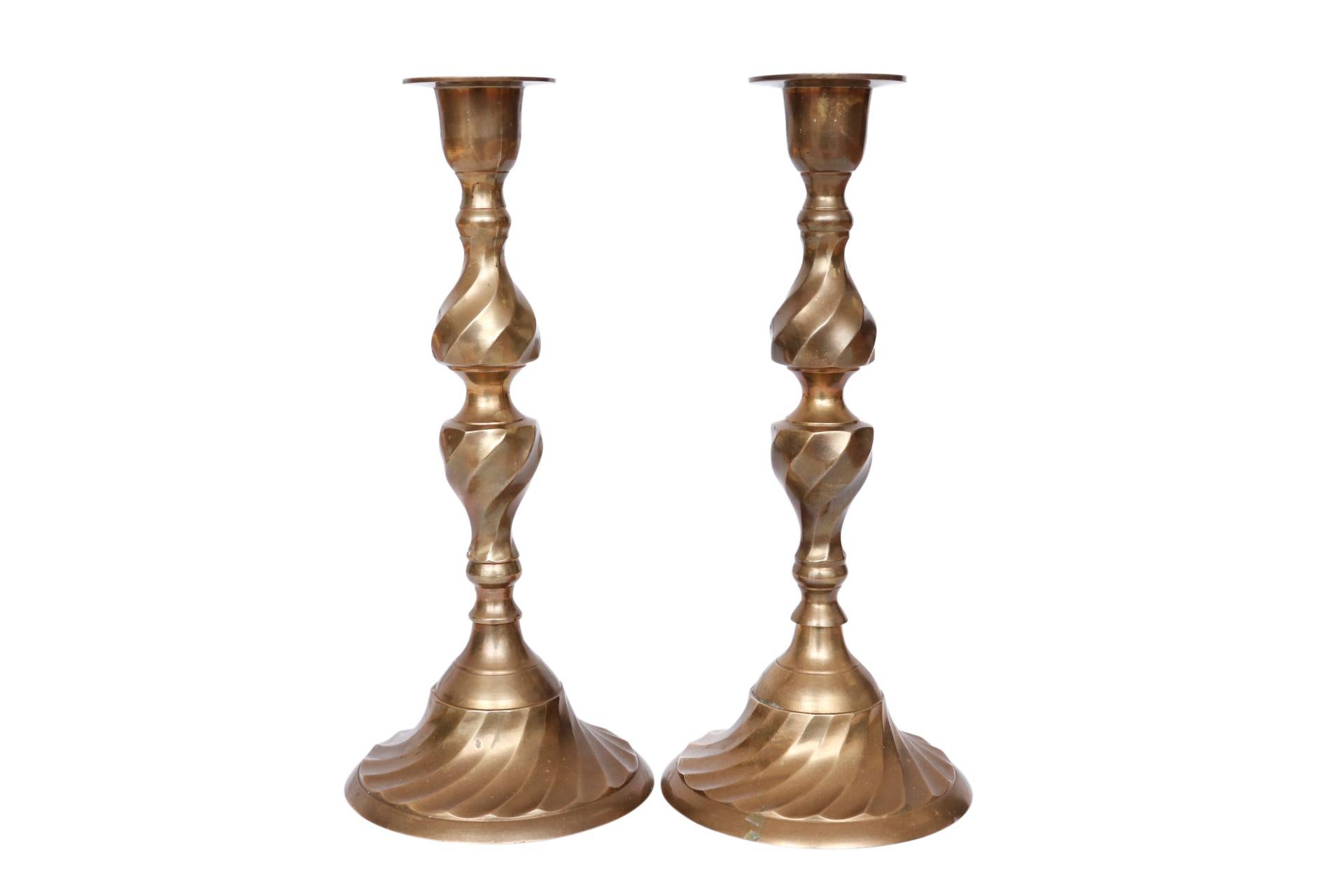 A pair of traditional brass candlesticks. Columns are turned with a double vase shape decorated with a square twist and a wide round base. Simple capitals have a small drip pan. Dimensions per candlestick.