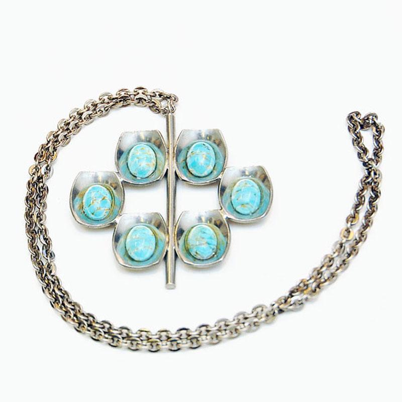 Wunderschöne Halskette aus türkisblauem Zinn von Jørgen Jensen, Dänemark, 1950er Jahre.
Der Anhänger hat sechs eiförmige Steine mit kupferfarbenen Details im Inneren der Steine. Jeder Stein ist von einer Zinnschale umgeben, die in der Mitte der