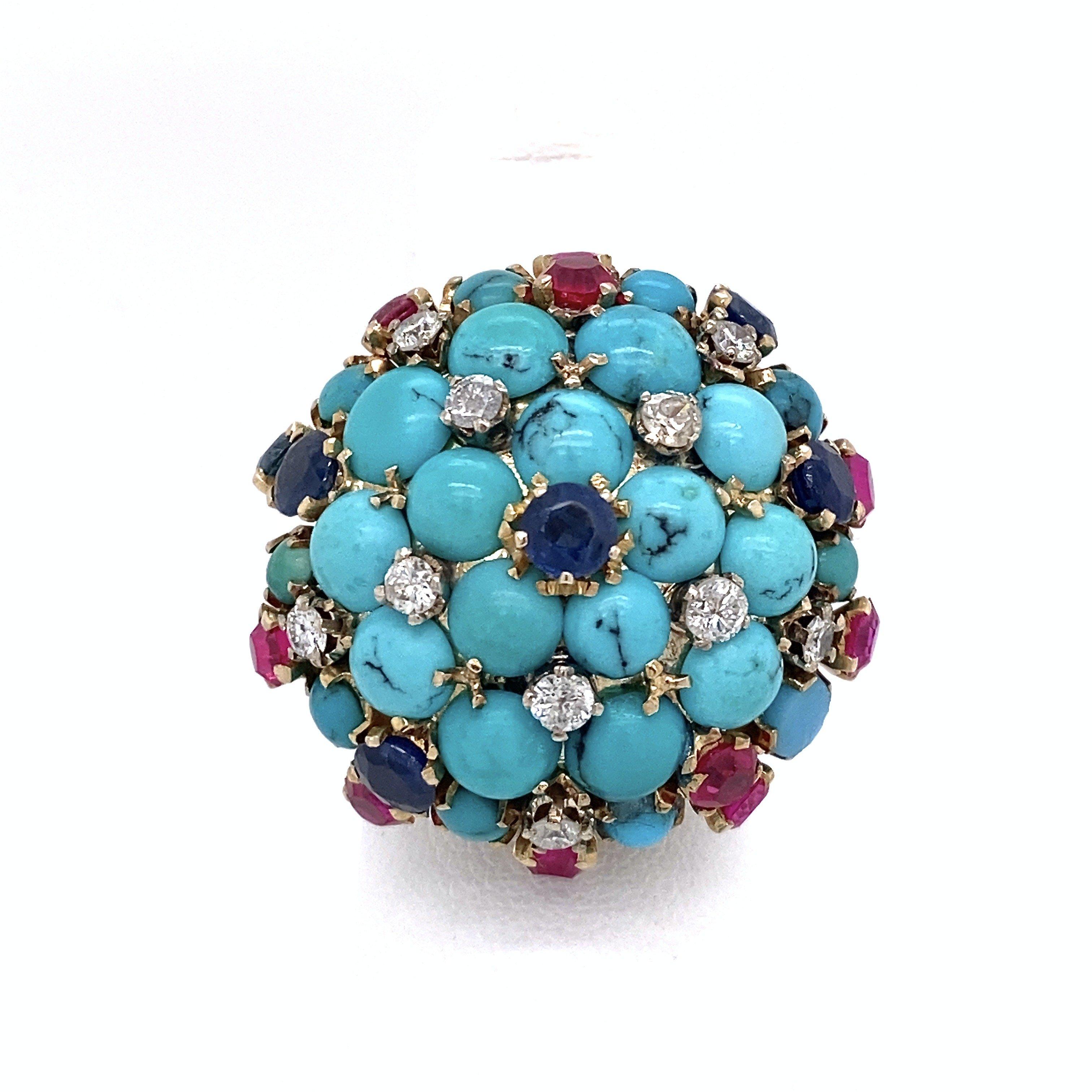 This vintage bombe ring dates from the 1950s and features an array of round, prong-set stones, including turquoise, diamonds, blue sapphires, and rubies set in 14KT yellow gold. The top of the ring is 27mm round, 13mm deep and the shank measures