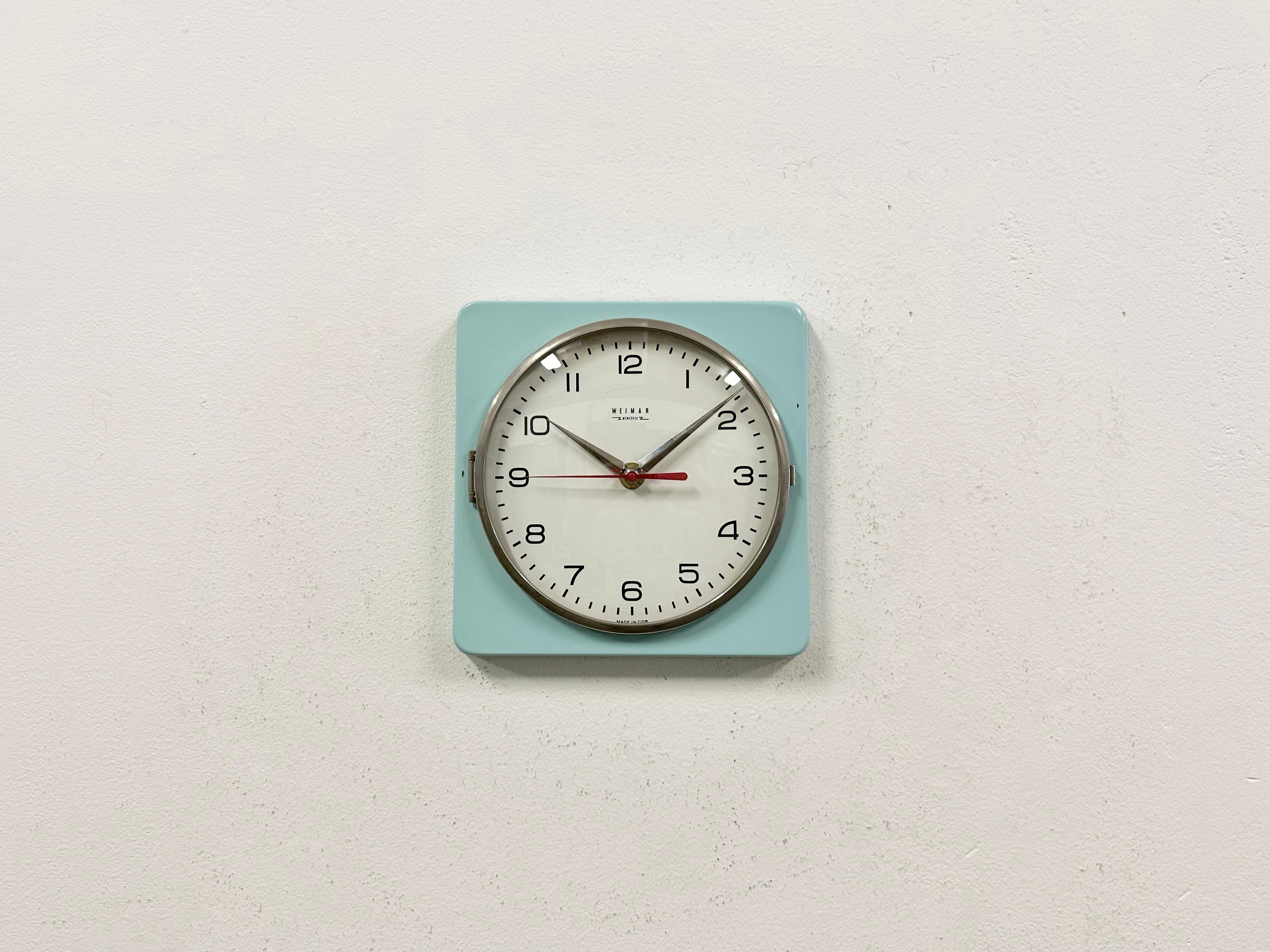 Vintage Industrial wall clock produced by Weimar Electronic in former East Germany during the 1970s. It features a turquoise iron body, an aluminium hands and a curved clear glass cover with brass frame.The battery-powered clockwork requires one AA