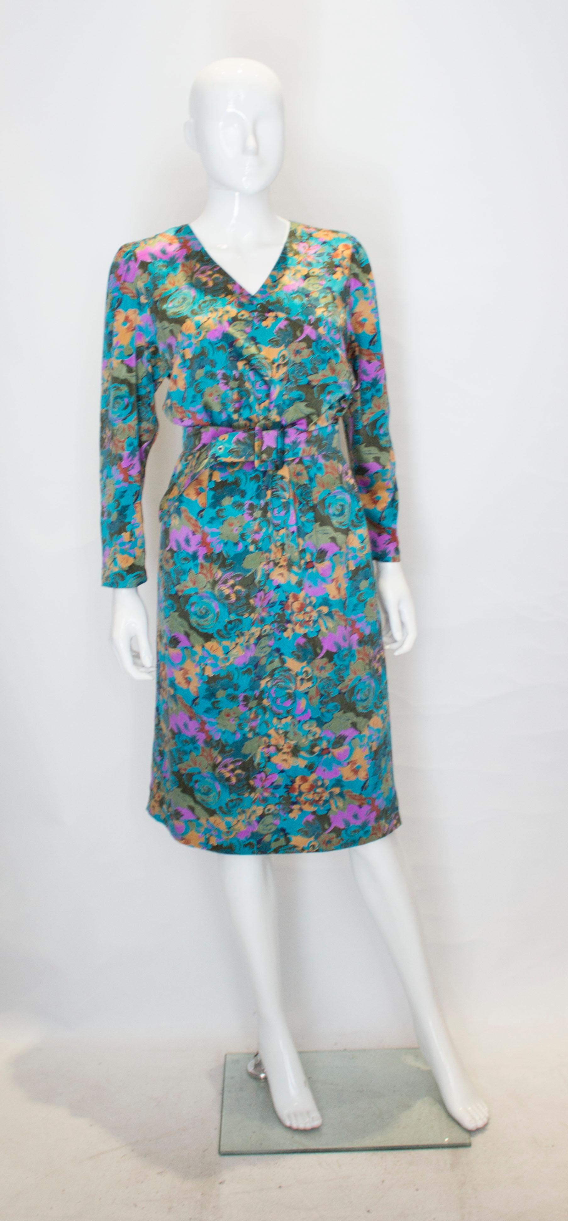 A pretty and easy to wear turquoise floral print day dress. The dress has a v neck wrap front neckline, self fabric belt and elbow length sleaves.  It open with a zip below waist leval  and fabric covered buttons above. It is fully lined.