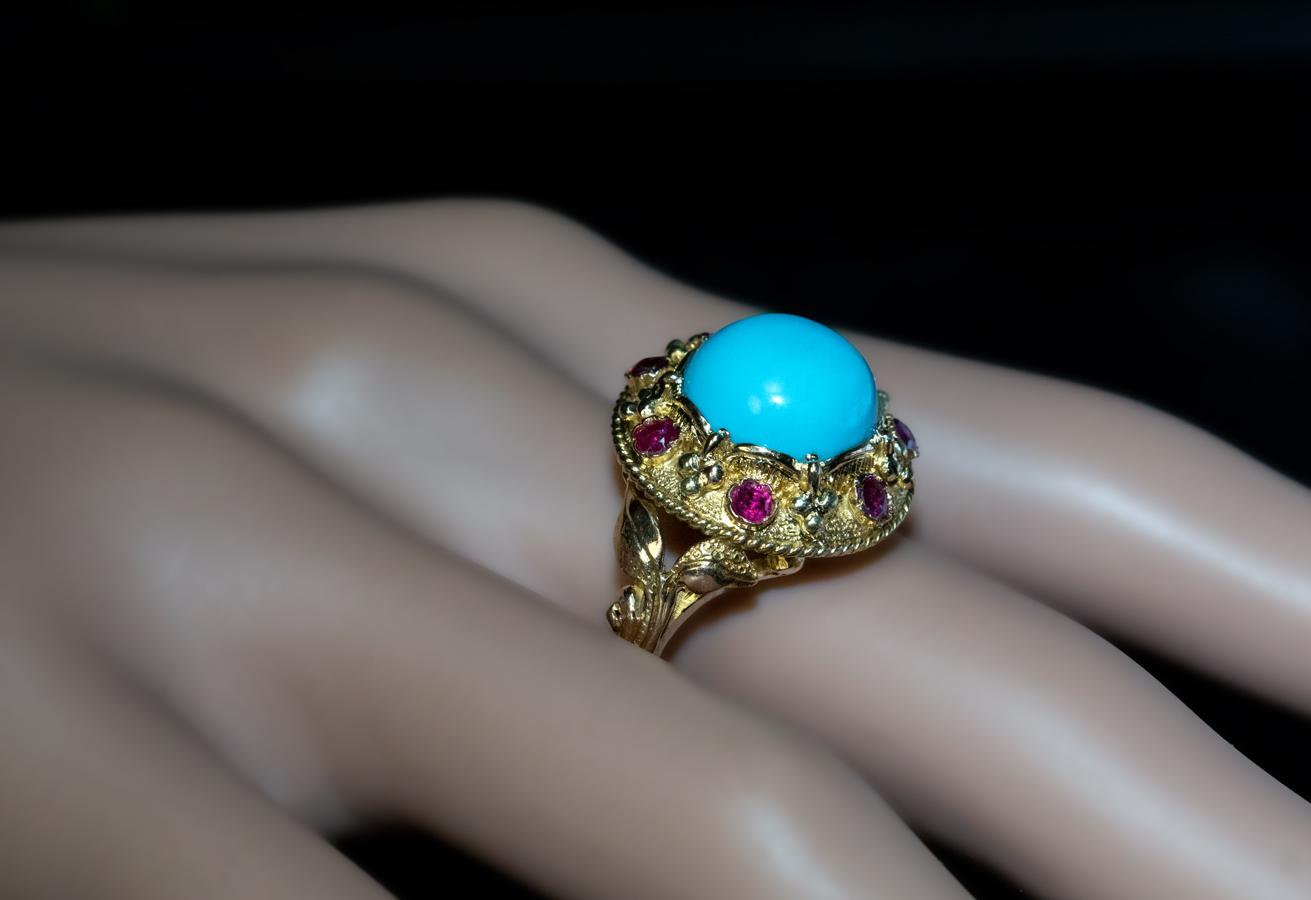 Circa 1950

The ring is finely modeled in 14K yellow gold and centered with a cabochon cut turquoise of an excellent sky blue color. The center stone is set in a textured gold bezel embellished with seven rubies and flanked by scrolling gold