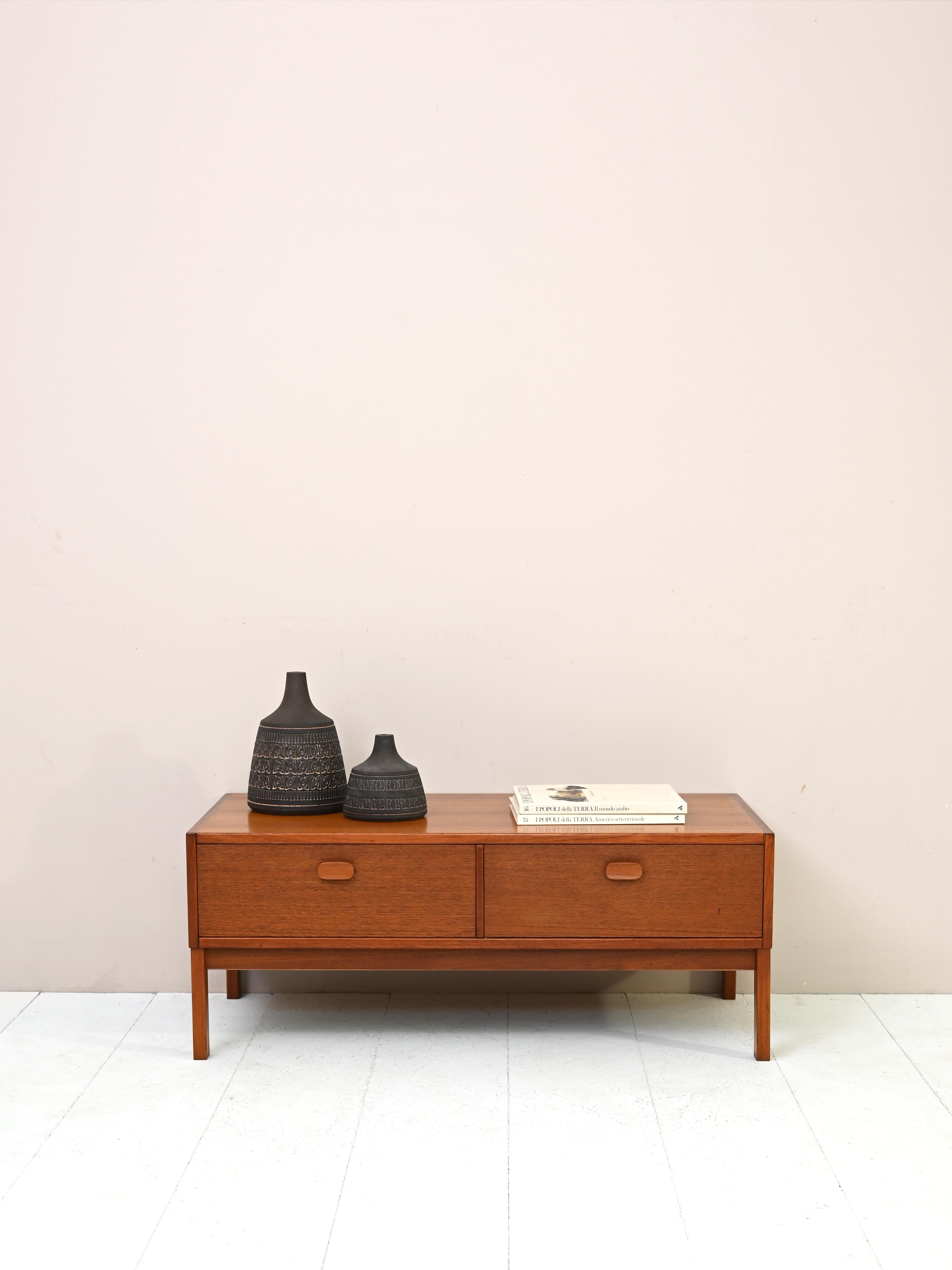 Low cabinet with drawers made of teak wood.
Produced by the Swedish company Ulferts this piece of furniture from the 1960s features a large top
shelf and two capacious drawers.
The dovetailing and wooden handle of the drawers hint at the quality