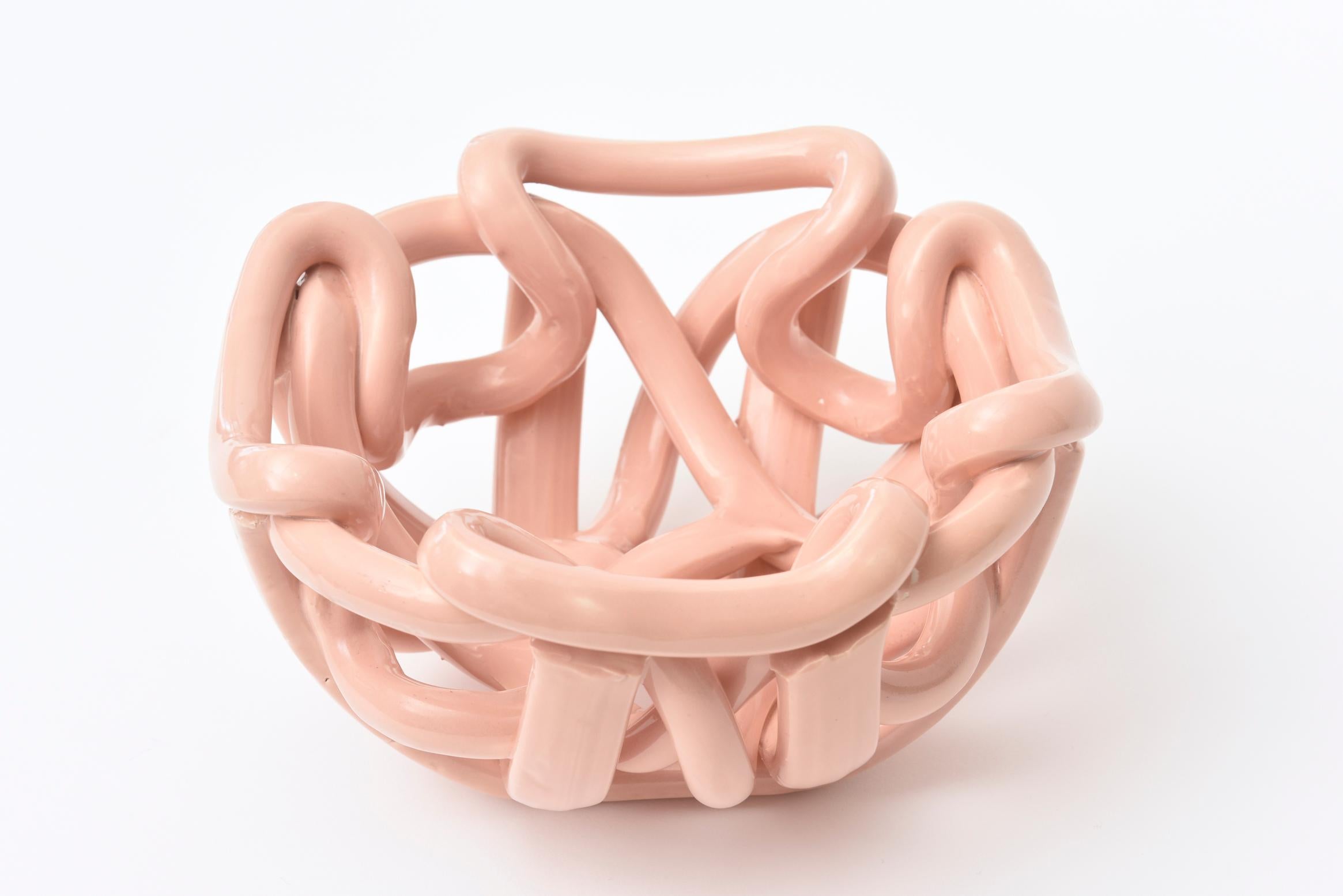 This lovely vintage glazed ceramic bowl has twists and turns of coiled ceramic. It is from the 1970s. The color is one of a dusty pink meets coral peach. The color looks retro and is organic modern. It is great as a decorative sculptural bowl for a