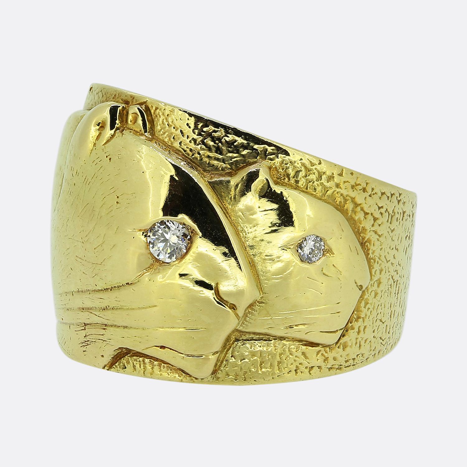 Ecco un anello a fascia unico, realizzato in oro giallo 18 carati. Questo pezzo vintage presenta una coppia di profili di pantera dettagliati, che si ergono collettivamente in cima a una fascia larga con finitura martellata. L'anello è poi