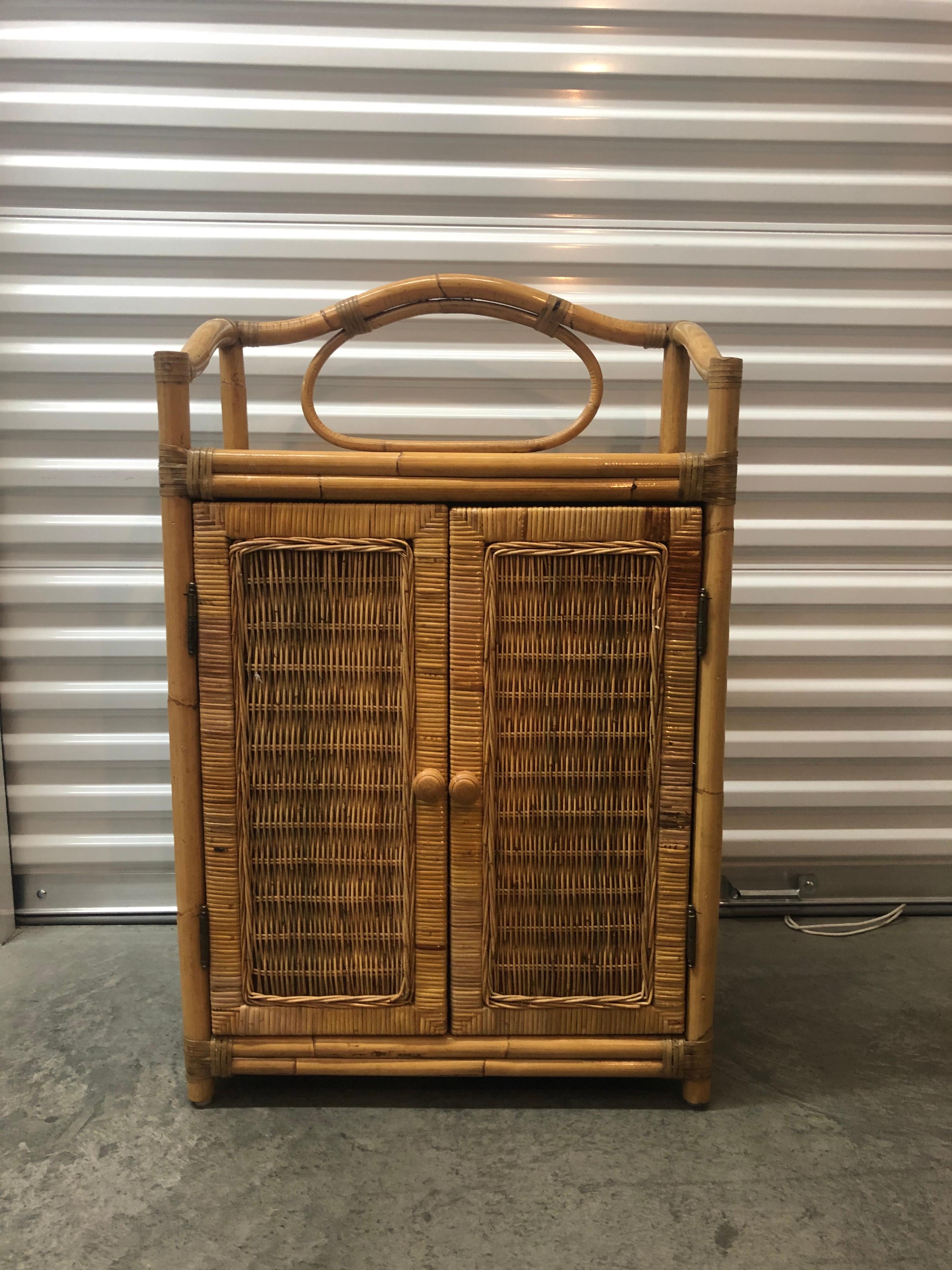 Vintage two-door bamboo and rattan bar cabinet.
Woven wicker details on sides and doors, wood knobs.
Two shelves inside. Finished with a nice bent bamboo top.
Size: 24. 1/4