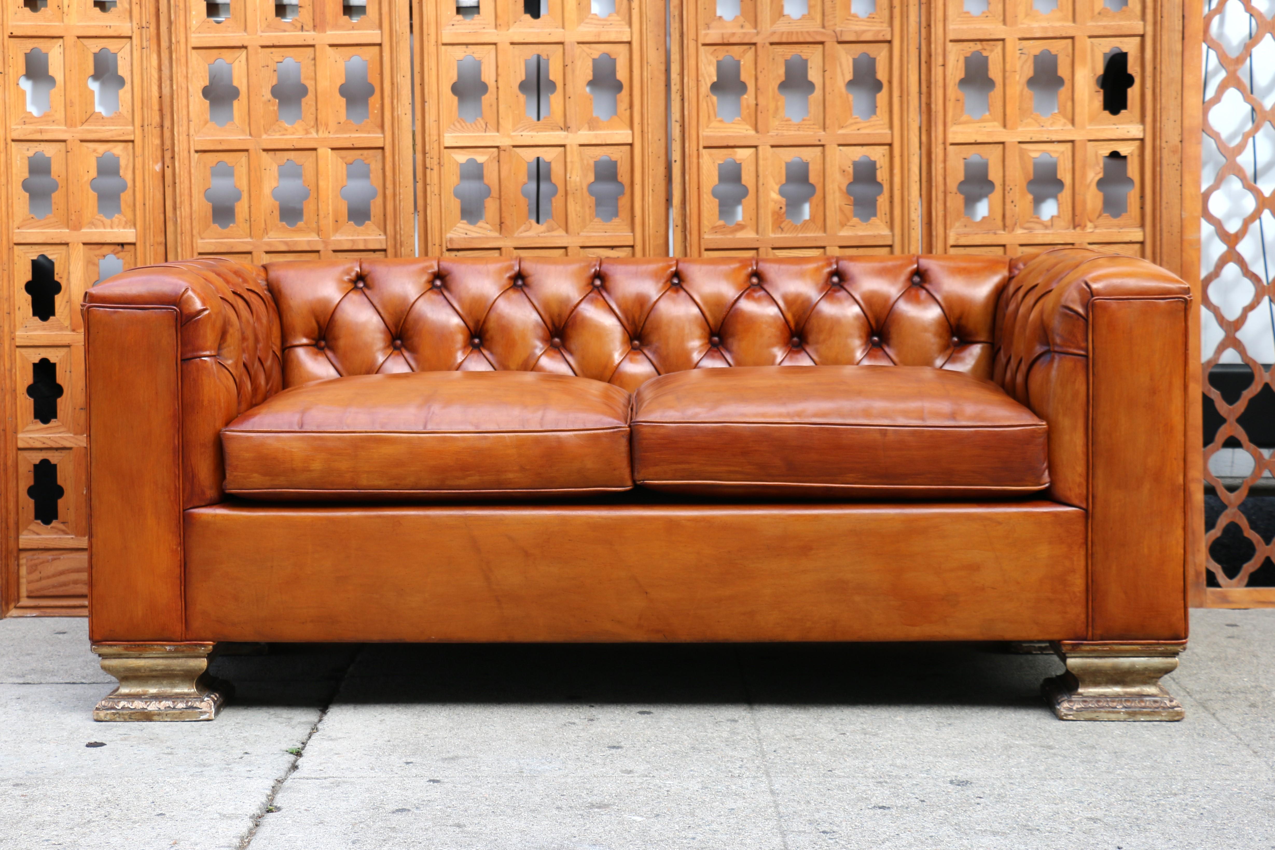 Splendido divano in pelle Chesterfield in buone condizioni vintage, i bottoni sono ben attaccati. È degli anni '90. È realizzato in pelle e gambe quadrate in legno con foglia d'argento. Ha braccia quadrate che hanno la stessa altezza dello