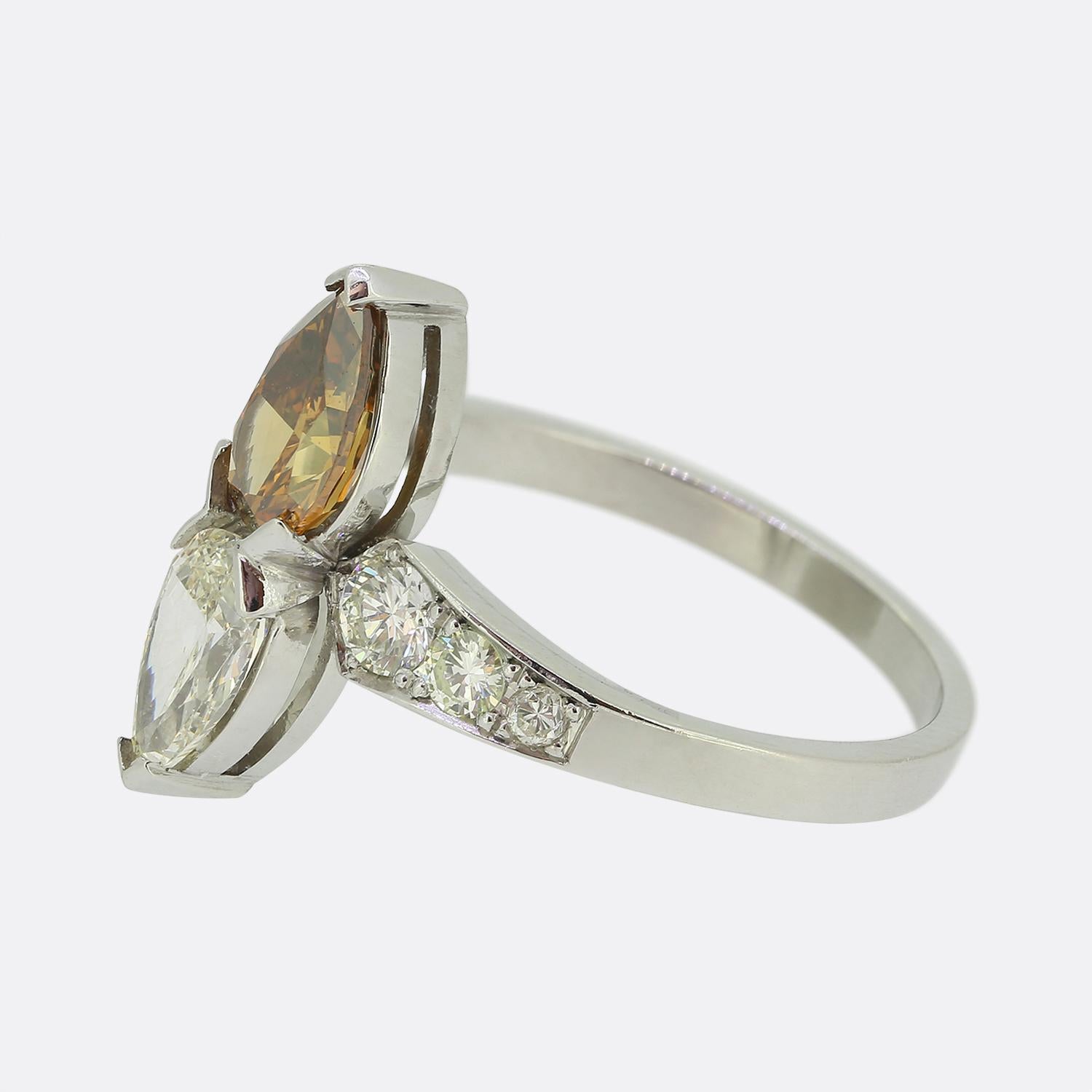 Here we have a beautiful two-stone diamond ring. This vintage piece features a duo of pair cut diamonds at the face; one fancy orange brown colour and the other white with a yellow tint. These radiant focal stones are then flanked and accentuated by