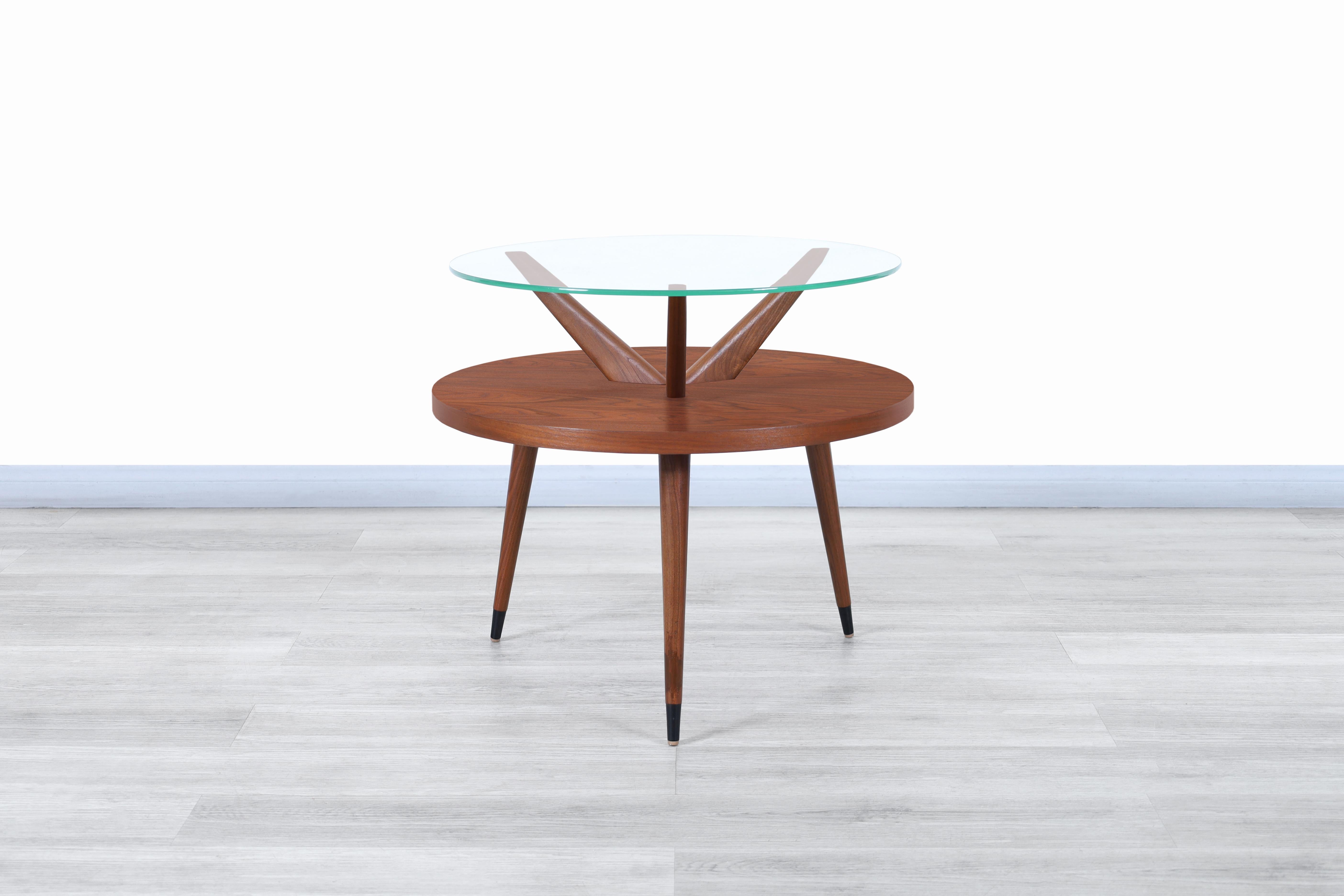Wunderschöner zweistöckiger Tisch aus Nussbaum und Glas, entworfen und hergestellt in den Vereinigten Staaten, ca. 1960er Jahre. Dieser Tisch zeichnet sich durch ein ganz besonderes Design aus, bei dem die Linienführung und die für die Konstruktion