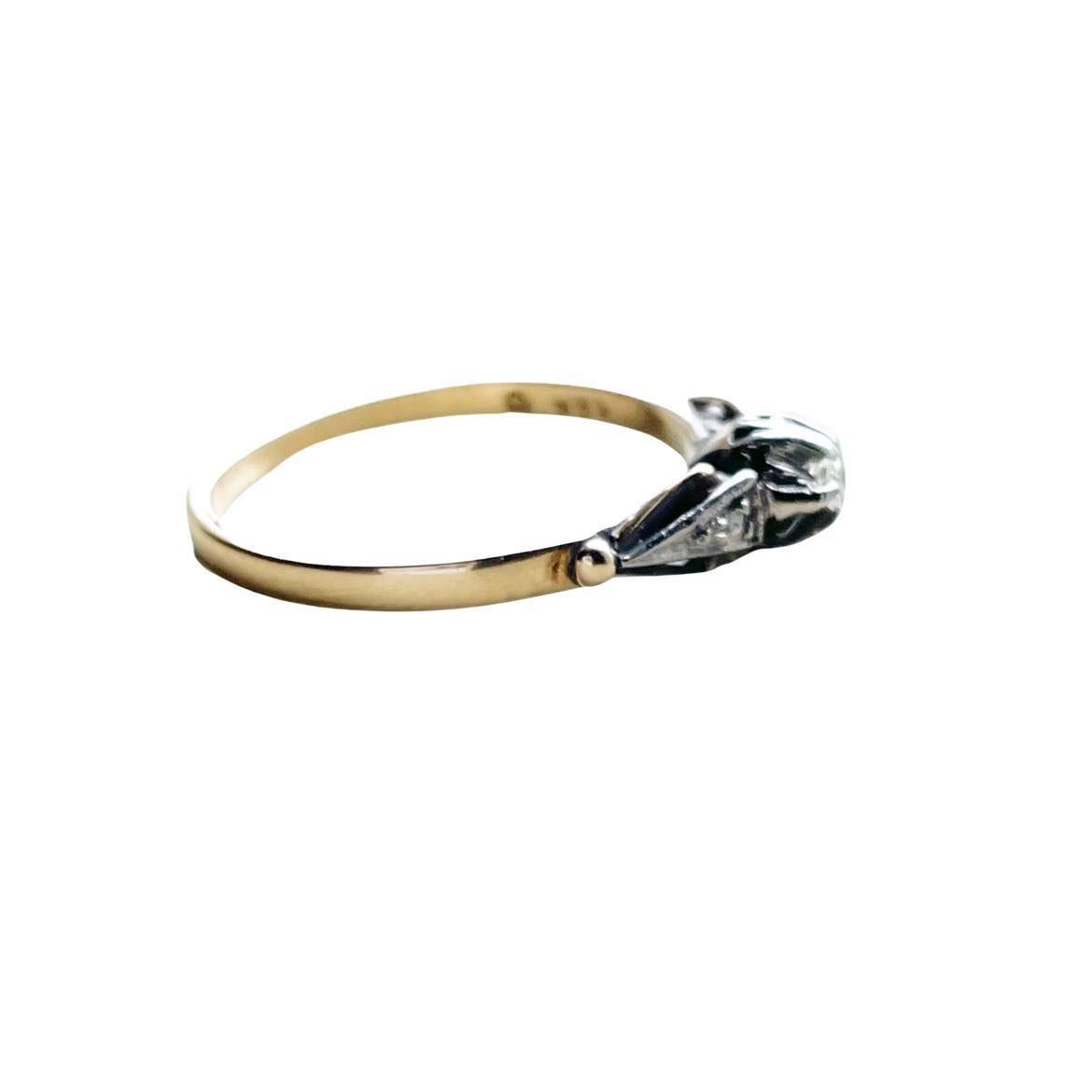 This dainty vintage beauty is crafted in 18K white gold and yellow gold. The classic smooth shank is yellow gold which intertwines with the white gold giving an elegant two tone look. In the center of the belcher setting is a round brilliant cut