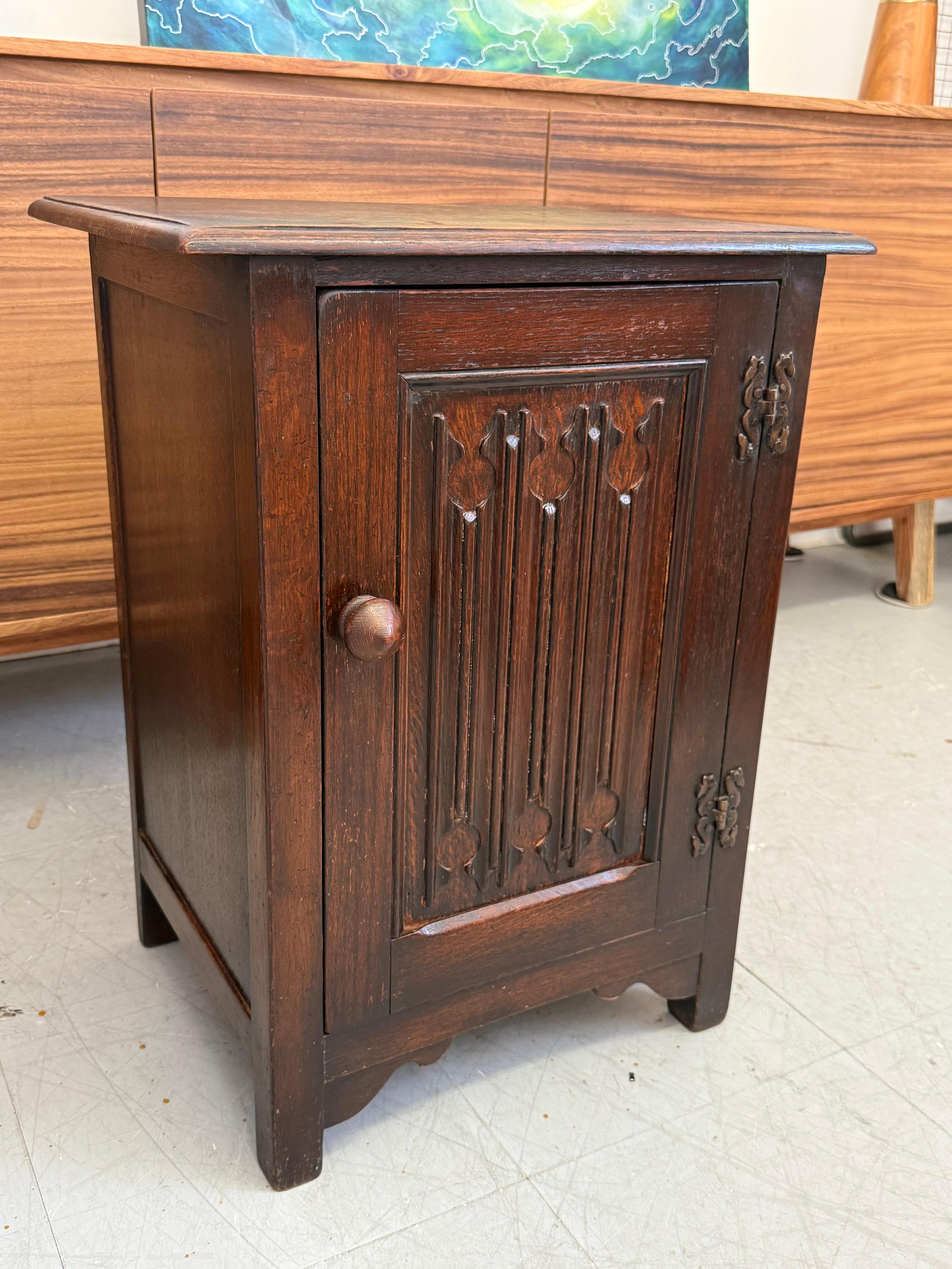 Meuble d'appoint vintage à forte influence galloise, avec un panneau avant profondément sculpté et une construction en chêne possiblement teinté foncé. La porte unique est ornée d'un quadrilobe vertical et d'un motif en forme de lancette, fréquents