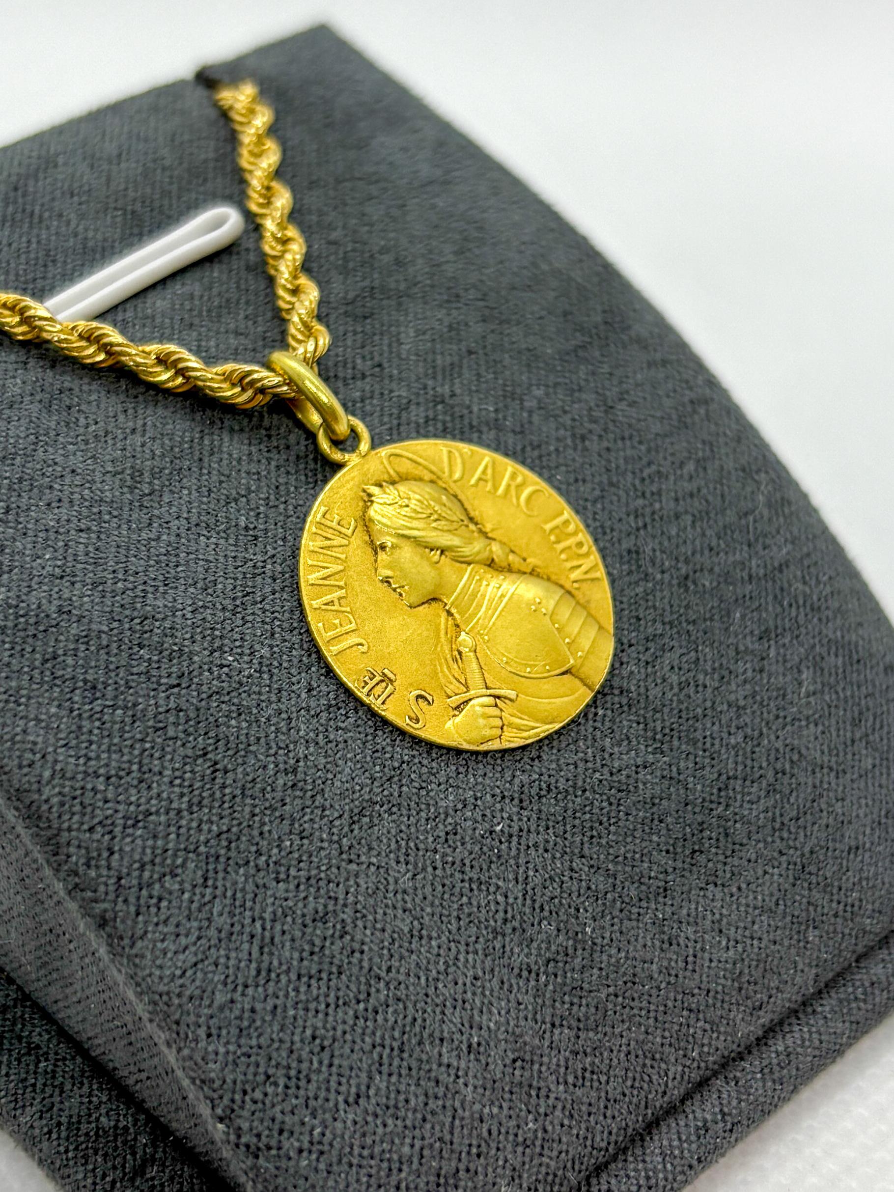 Eccezionale medaglia in oro giallo 18k che raffigura Sainte Jeanne d'Arc con notevole precisione. Il dritto mostra la santa in armatura completa, con i capelli splendidamente intrecciati, incorniciata dall'iscrizione 