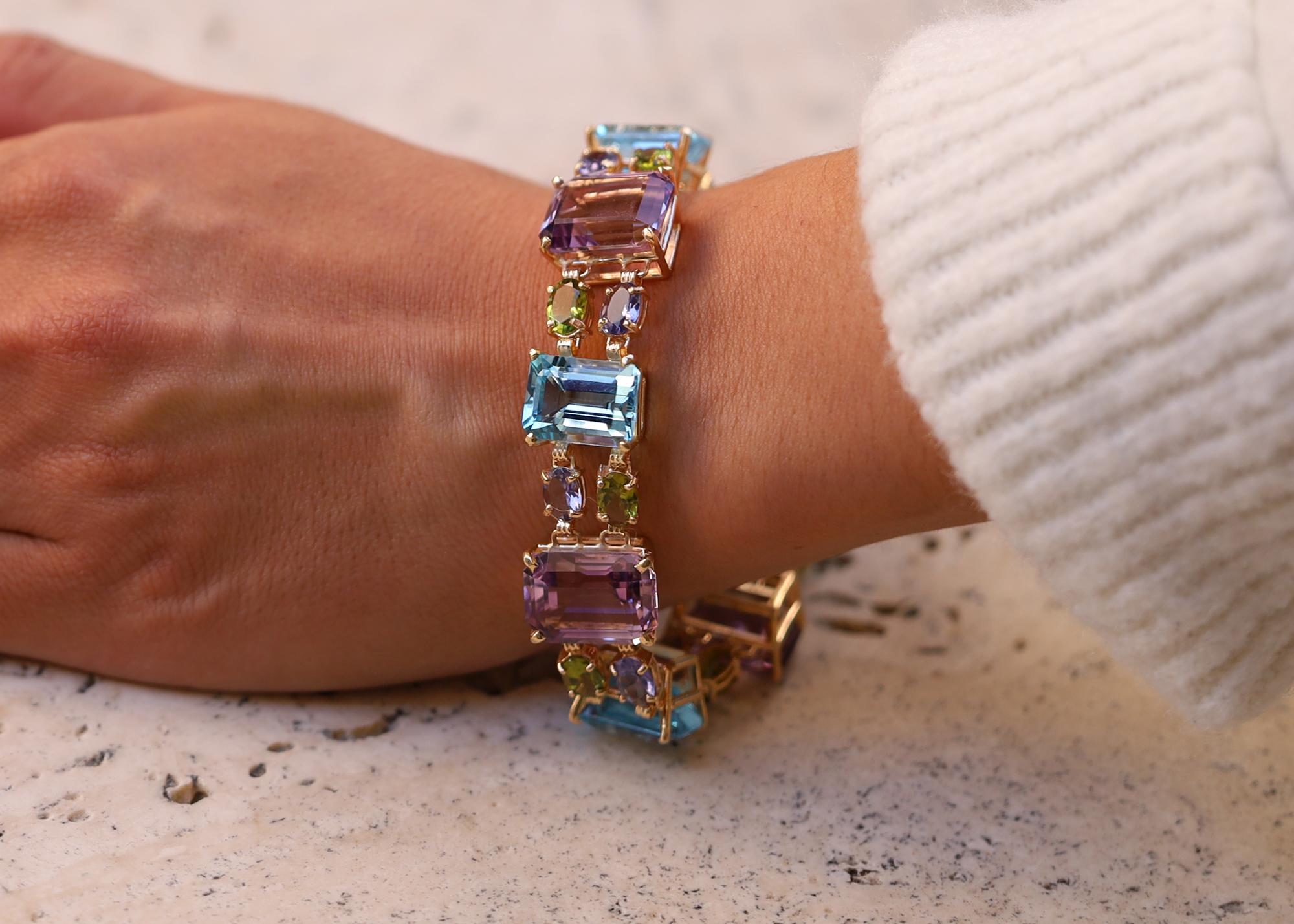 An authentic vintage 1980's rainbow gemstone unisex bracelet. 14 karat yellow gold links embrace nearly 100 carats of royal purple amethysts, vivid blue topaz alternating with peridot and iolite links. Presenting Indian hallmarks with expert