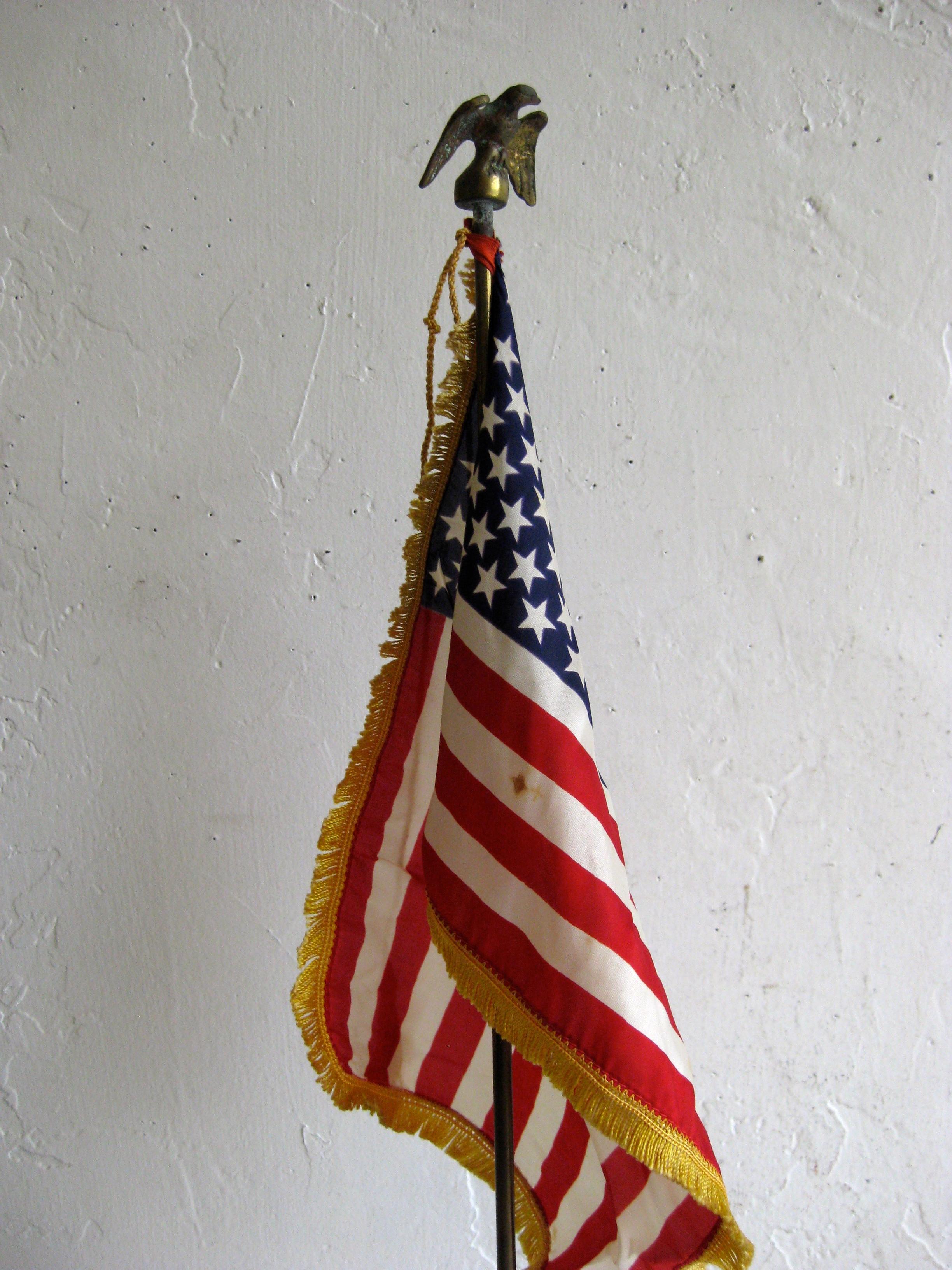 Very unique vintage military desk top 50 star American flag and solid brass flagpole. The brass flagpole appears to be older and has an eagle on the top. Flag dates from the late 1950s to early 1960s/ The silk flag has a gold fringe. Brass has a