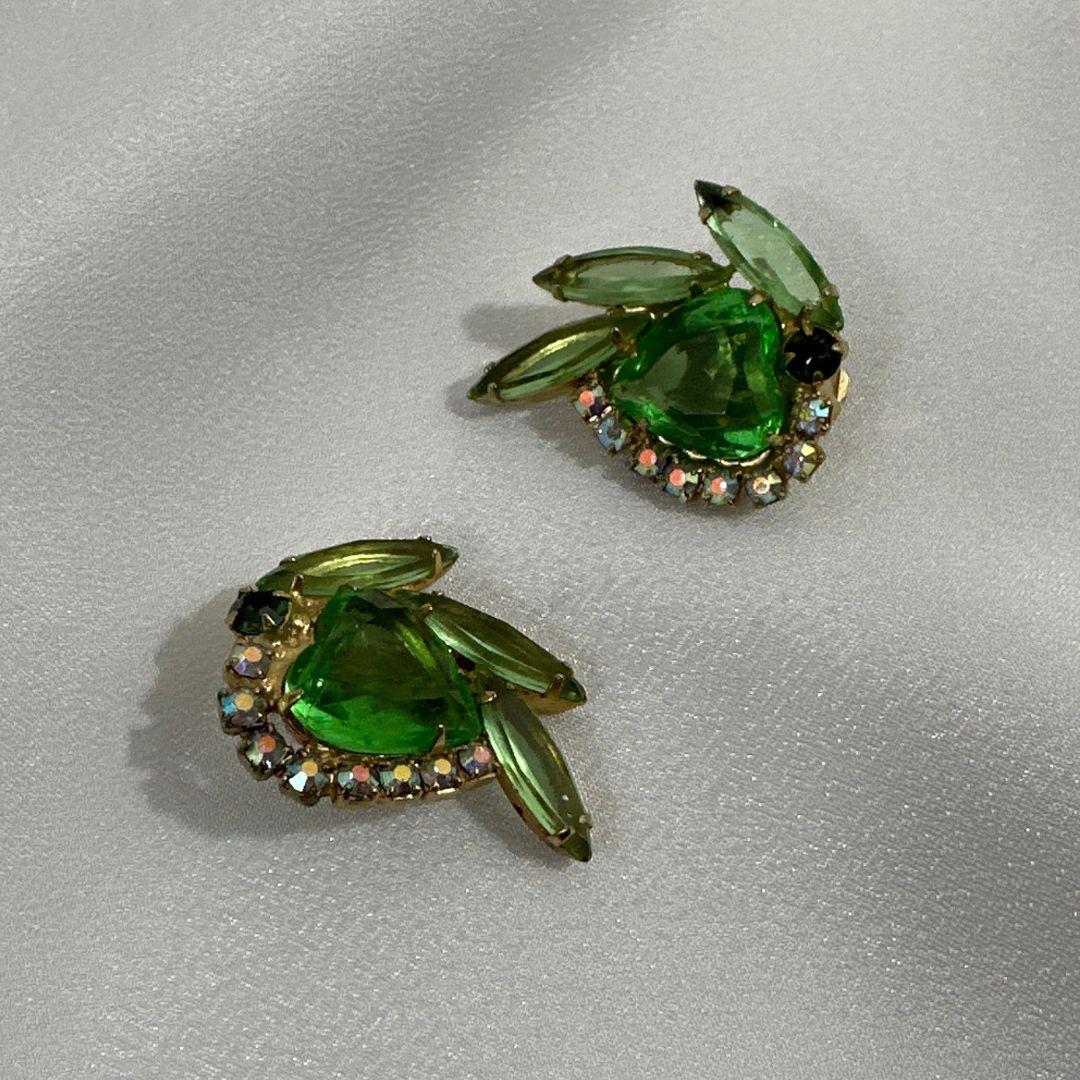 Earring Length: 1.25″

Bin Code: E1 / P2

Step into the world of vintage allure with these Vintage Unsigned Julianna Green Heart Cut Glass and Rhinestone Earrings. These exquisite earrings combine the elegance of heart-shaped green cut glass stones