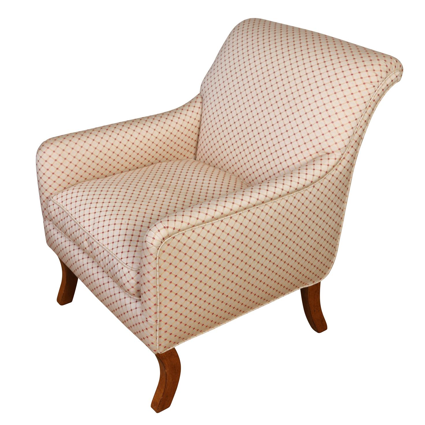 A vintage upholstered club chair in modern style with a flared back, narrow arms and slender light wood legs. Fabric upholstery is a neutral cream ground with a red and gold diamond geometric design. Chair is made by A. Rudin.