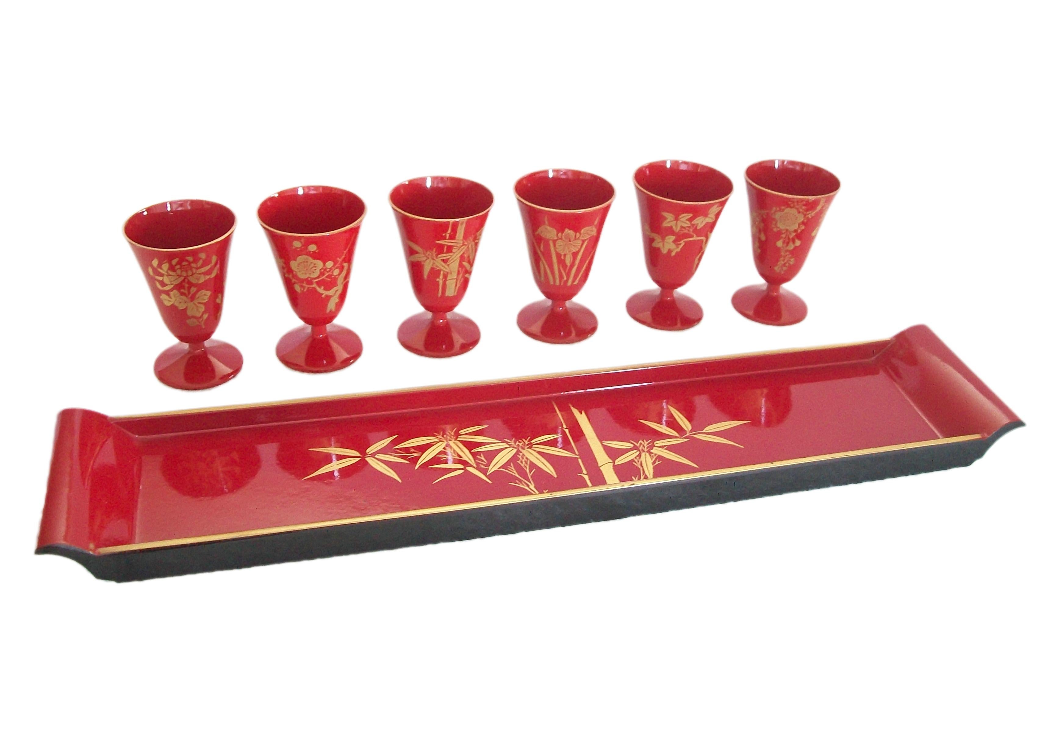Vintage Urushi red lacquer tray with six stemmed cups - each cup gilt decorated with a different floral, leaf or bamboo specimen - the tray gilt decorated with bamboo to the center, the underside black lacquer - makers label to the outside of the
