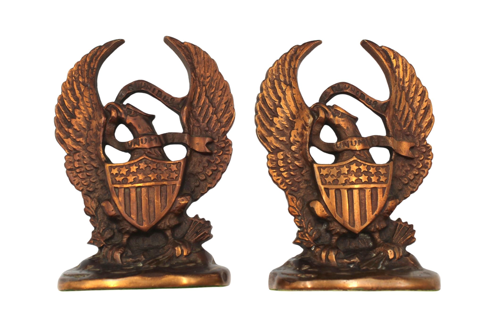 Offered is a vintage set of brass bookends featuring an eagle with widely spread wings. The eagle holds arrows and an olive branch in its talons and appears with a large shield against its chest. The eagle carries a banner in its mouth that reads 