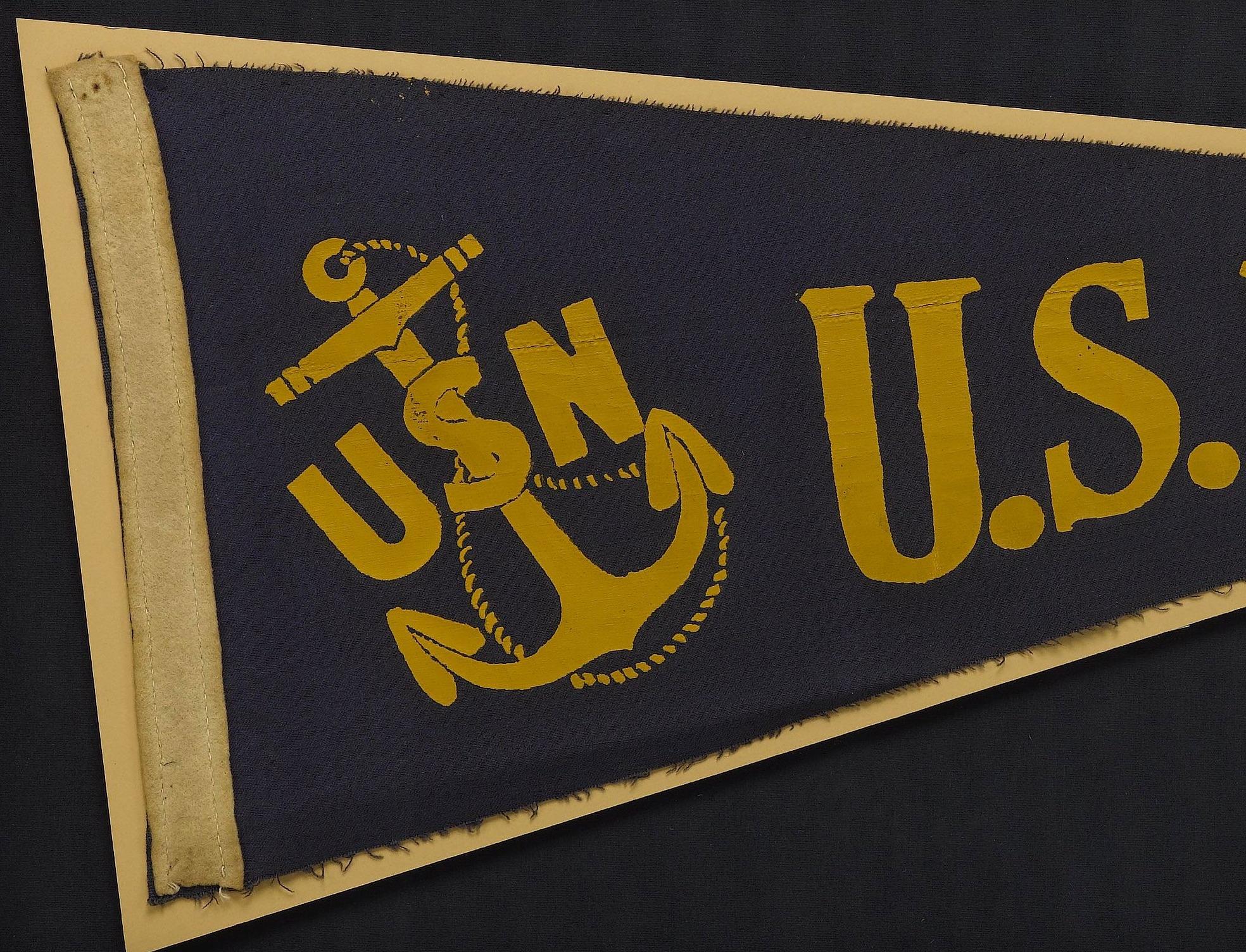 Presented is a vintage U.S. Navy felt pennant, from the early 1940s. This WWII era pennant is constructed of dark blue felt with yellow printed lettering. The pennant has a white felt headband, which is sewn on with a running stitch. The pennant